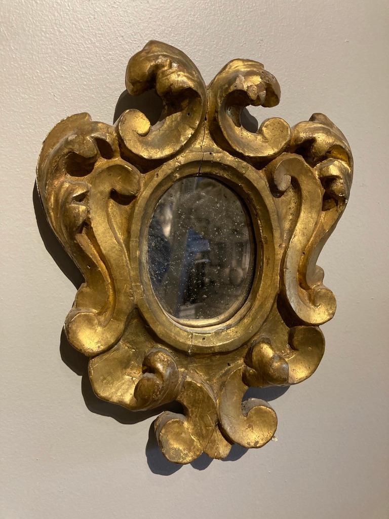 A lovely pair of Italian gilt wood mirrors in the 18th century Baroque style. These diminutive frames are beautifully carved and fitted with 'antiqued' mirror glass. Perfect accent pieces for a bathroom, bedroom or entryway. 10 high by 8 inches wide.