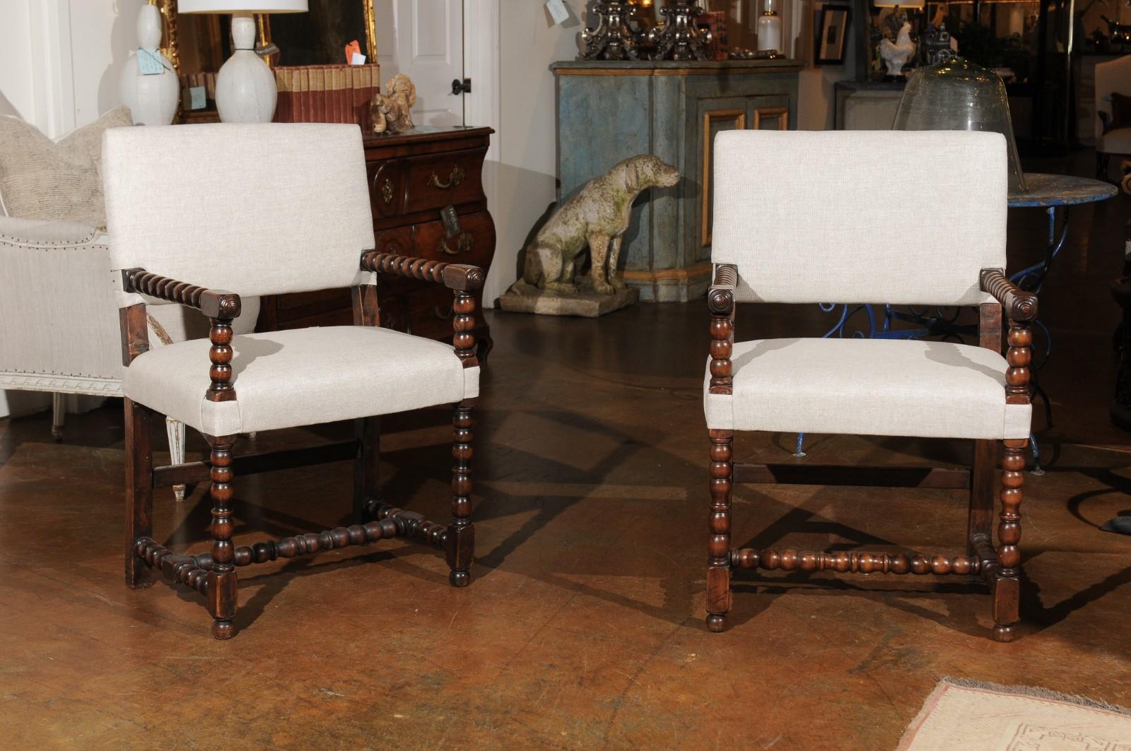 A pair of Italian Baroque style oak armchairs from the 19th century, with bobbin arms, legs, cross stretcher and new upholstery. Born in Italy during the 19th century, each of this pair of armchairs features an elegant linear silhouette. The backs