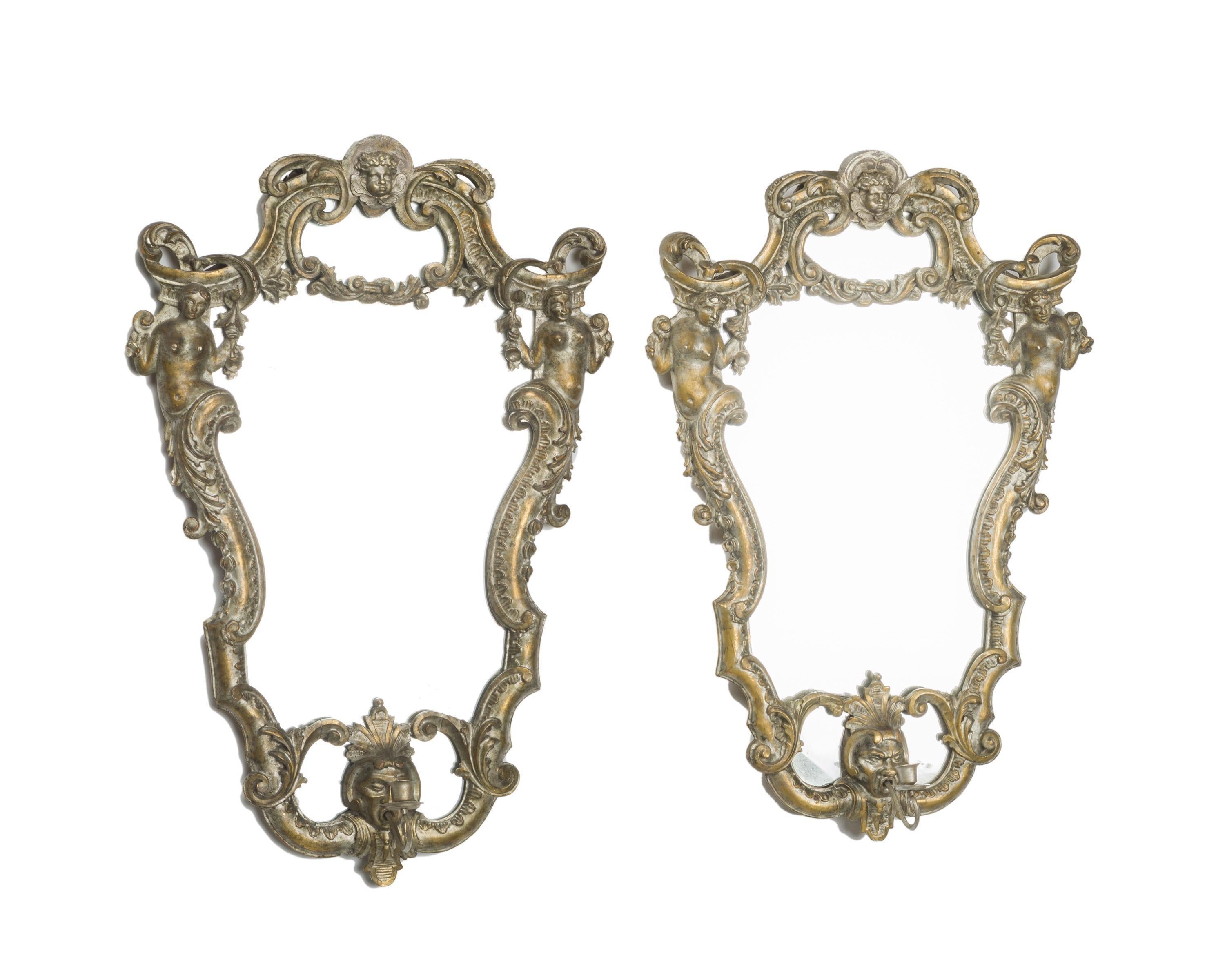 A exquisite pair of Italian Baroque style silver leafed carved wood girandole mirrors, 19th century.
The silver-leafed cartouche mirrors are surmounted with a scrolled crest centered by a putti mask, flanked by two hand carved maidens within a