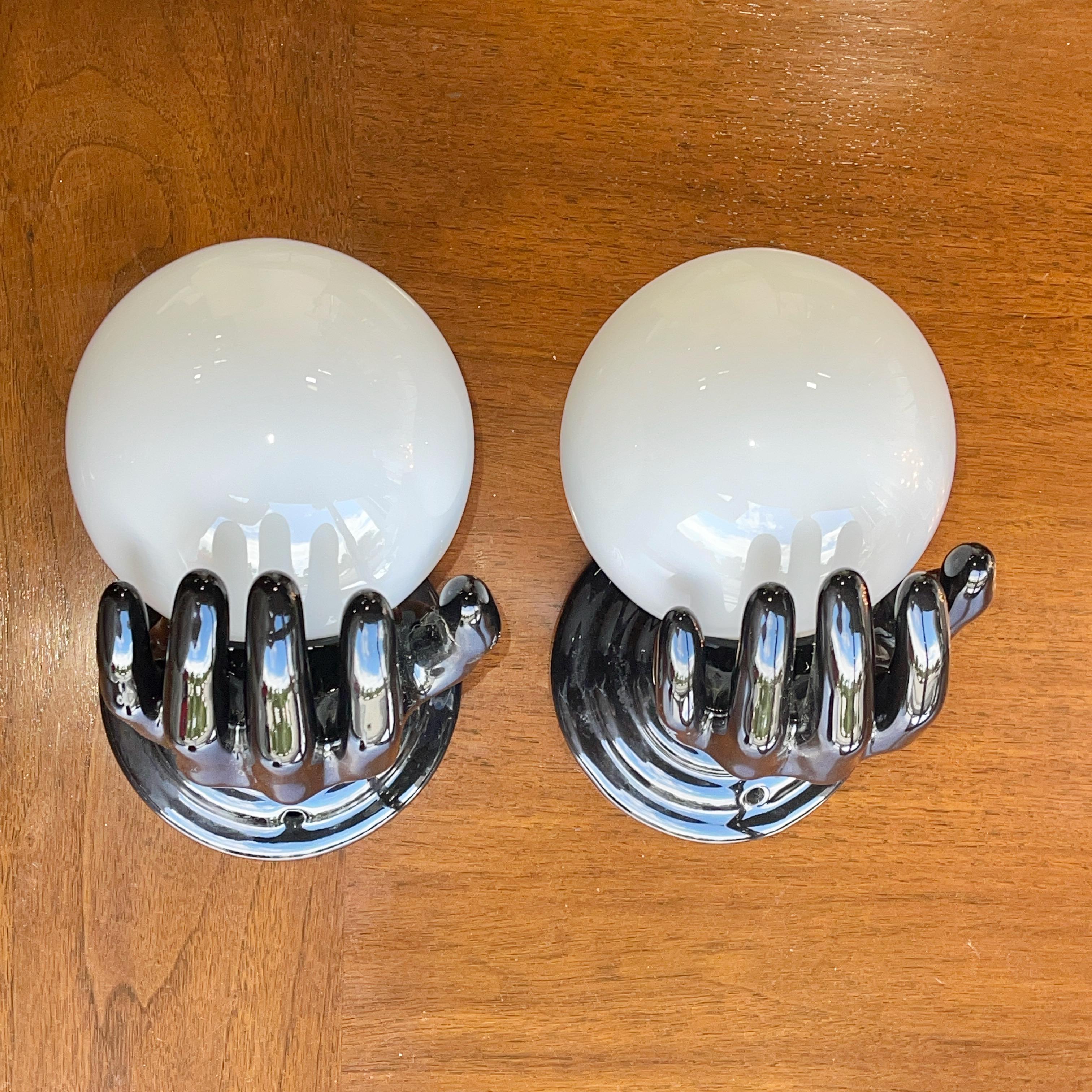 Coppia di lampade da parete in ceramica smaltata nera degli anni '60 a forma di mano aperta (destra) che regge un globo di vetro bianco su una singola presa a candelabro che può contenere una lampadina da 60 watt. Può essere cablata o con cavo.