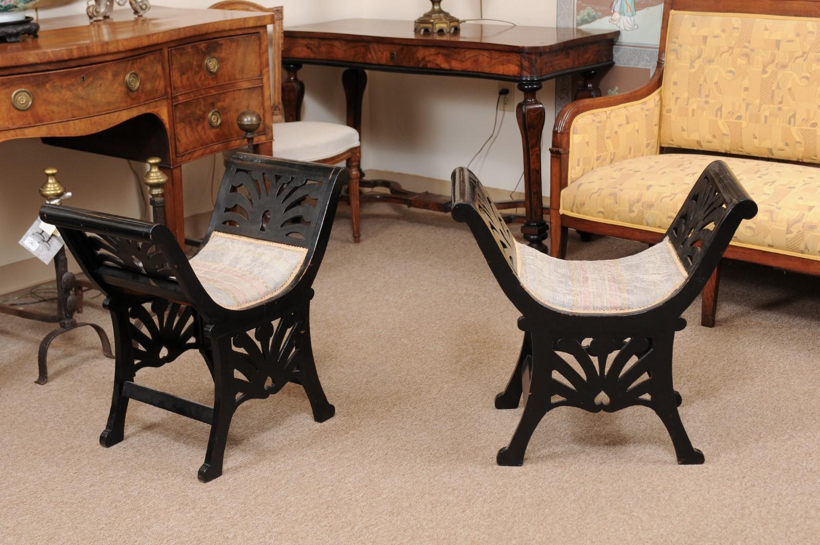 A pair of early 20th century Italian window benches with saddle seat, pieced carved arms and apron in the same design ending in spayed legs joined by stretchers and rounded feet.