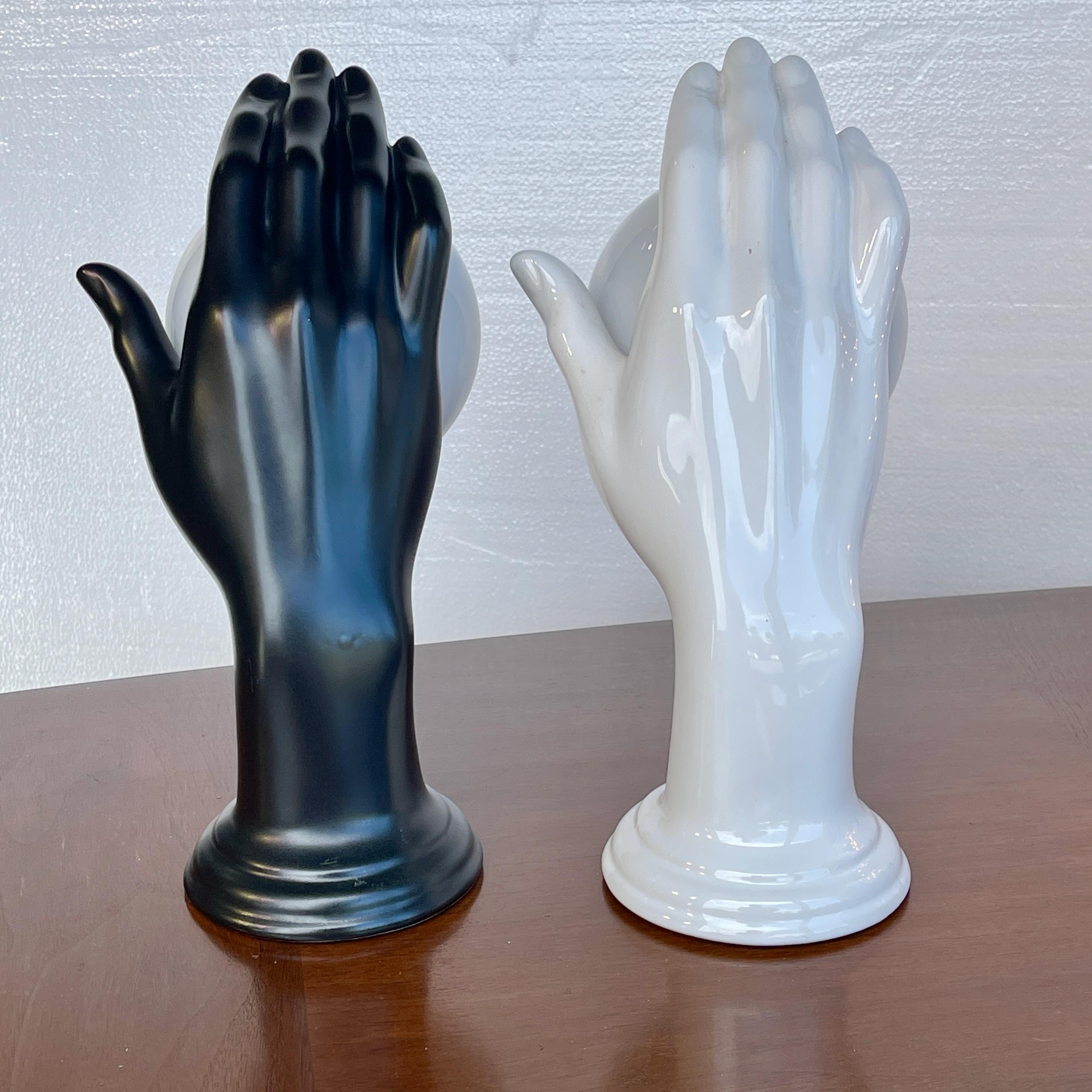 Pair of 1960's Italian black and white ceramic wall mounted lamps in the form of an open (right) hand holding a white glass globe over a single candelabra socket which holds up to a 60 watt bulb. Can be hard wired or corded.