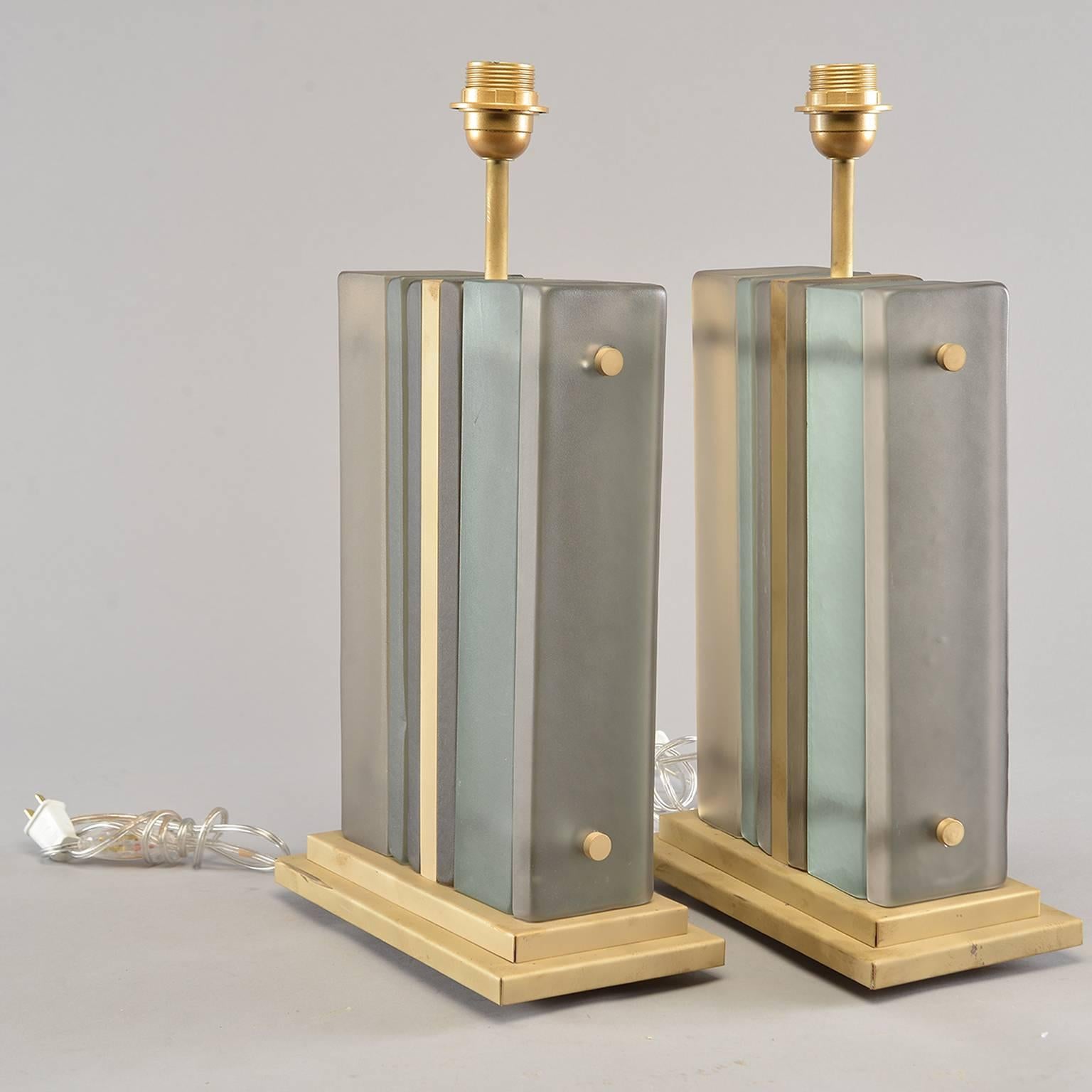 Pair Italian table lamps have bases with layers of art glass in shades of pale blue green and taupe sandwiched together with gilt metal hardware, circa 1990s. Unknown maker. Both lamps have been rewired for US electrical standards. Sold and priced