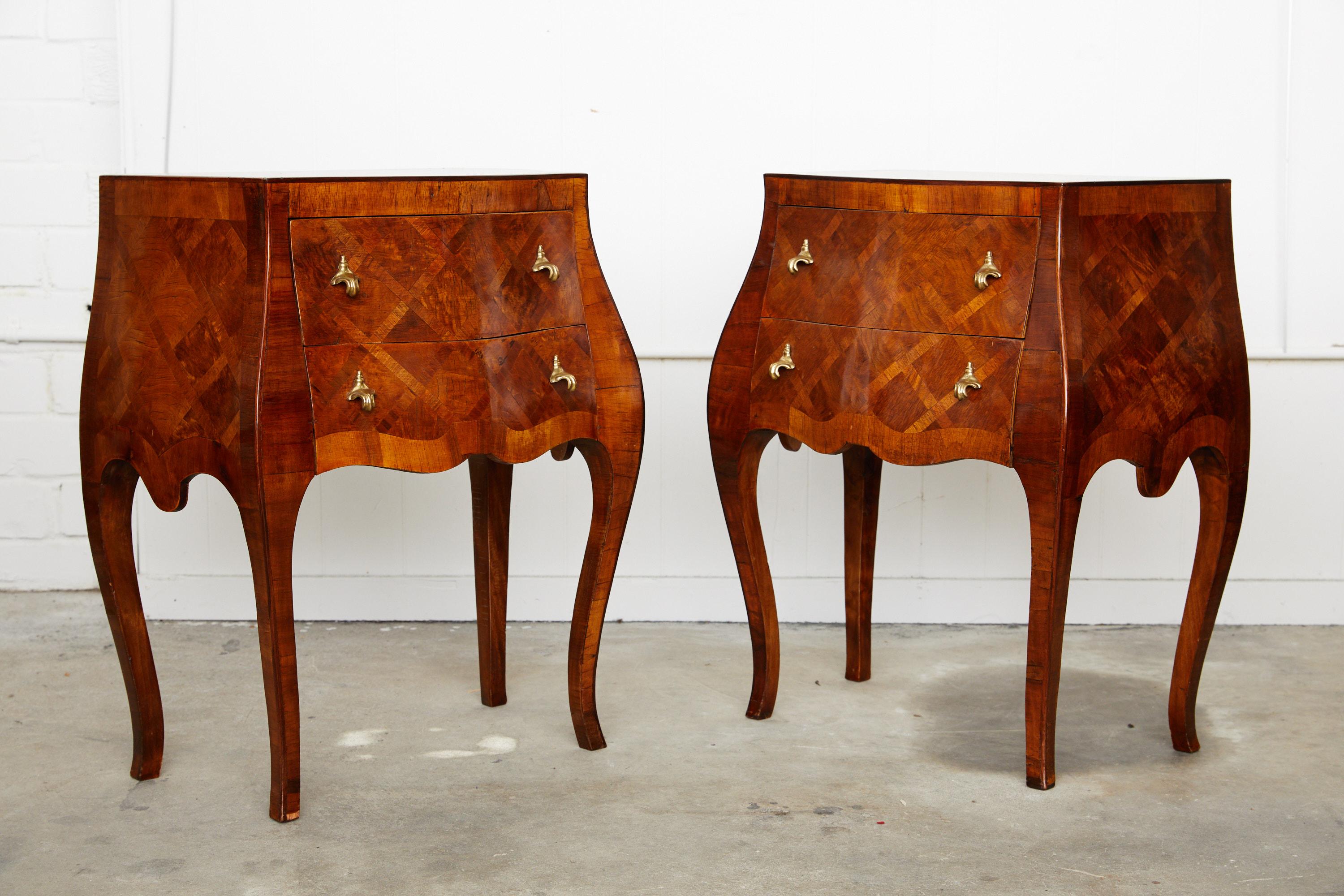 20th century pair of Italian commodinis or end tables in a bombe form holding two drawers, each with rococo style brass hardware. The tables are decorated in a marquetry inlay.