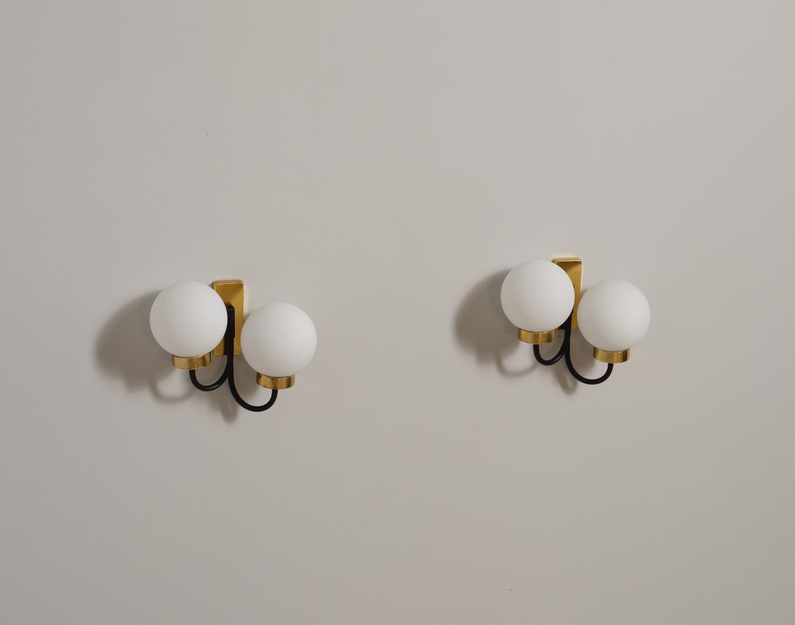 Pair of Italian brass and black-enameled steel wall sconces dating to the 1950s, each formed by a rectangular backplate in lightly patinated brass that supports two curved enameled arms terminating in uniform opaline glass globes; every fixture