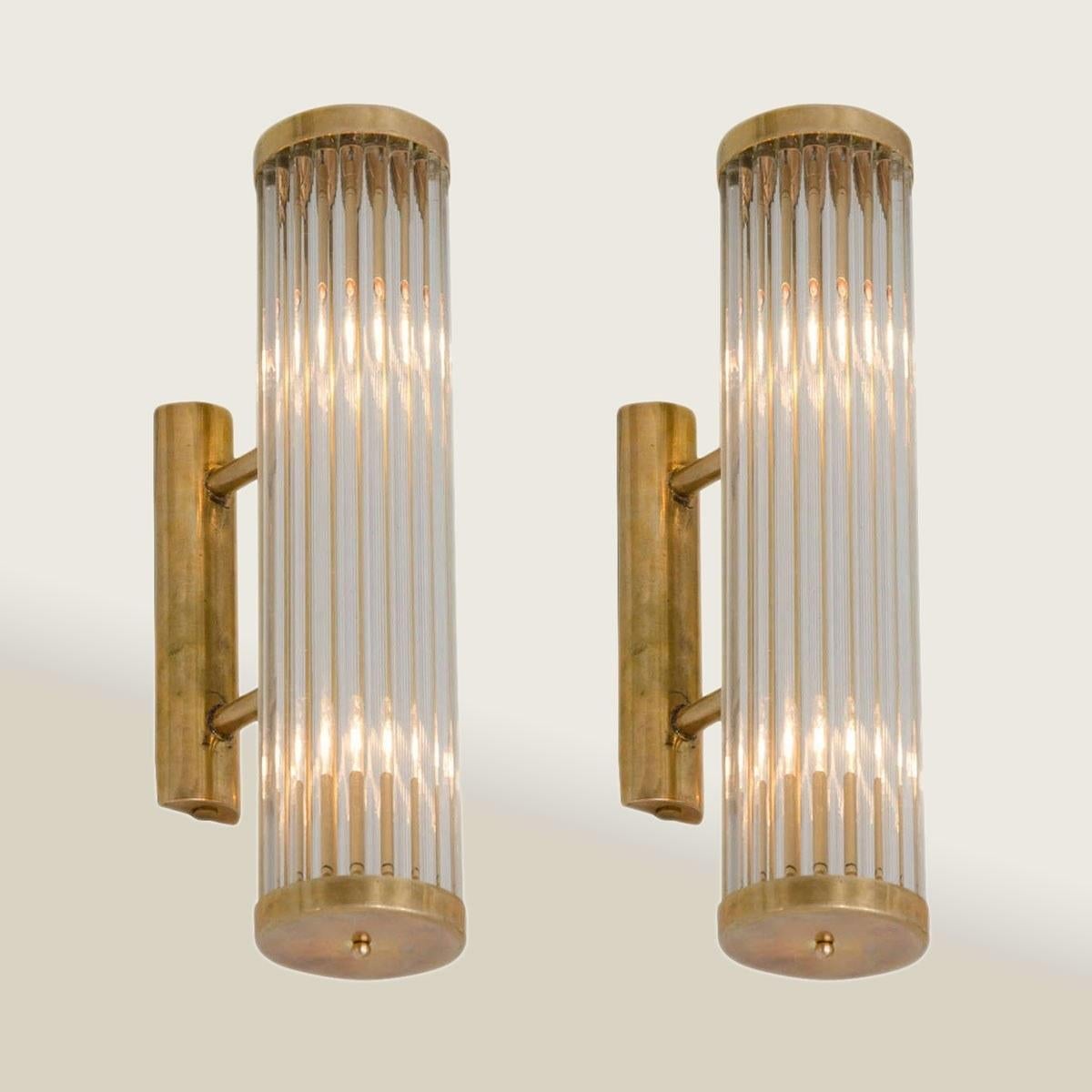 Contemporary Art Deco inspired Italian wall lights in the style of ‘Venini’.
Each light comprises of a circle of slim Murano glass rods capped top and bottom by round brass plates that attach with two slim brass arms to a brass wall bracket.
Two 