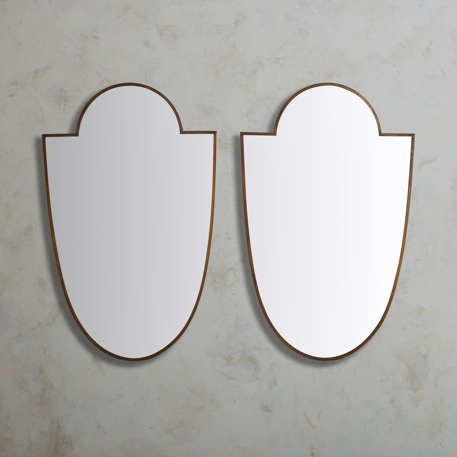 A pair of large scale vintage Italian shield shaped wall mirrors with delicate patinated brass frames. These mirrors have wooden backings and hardware for hanging. Sourced in Italy, 20th Century.

