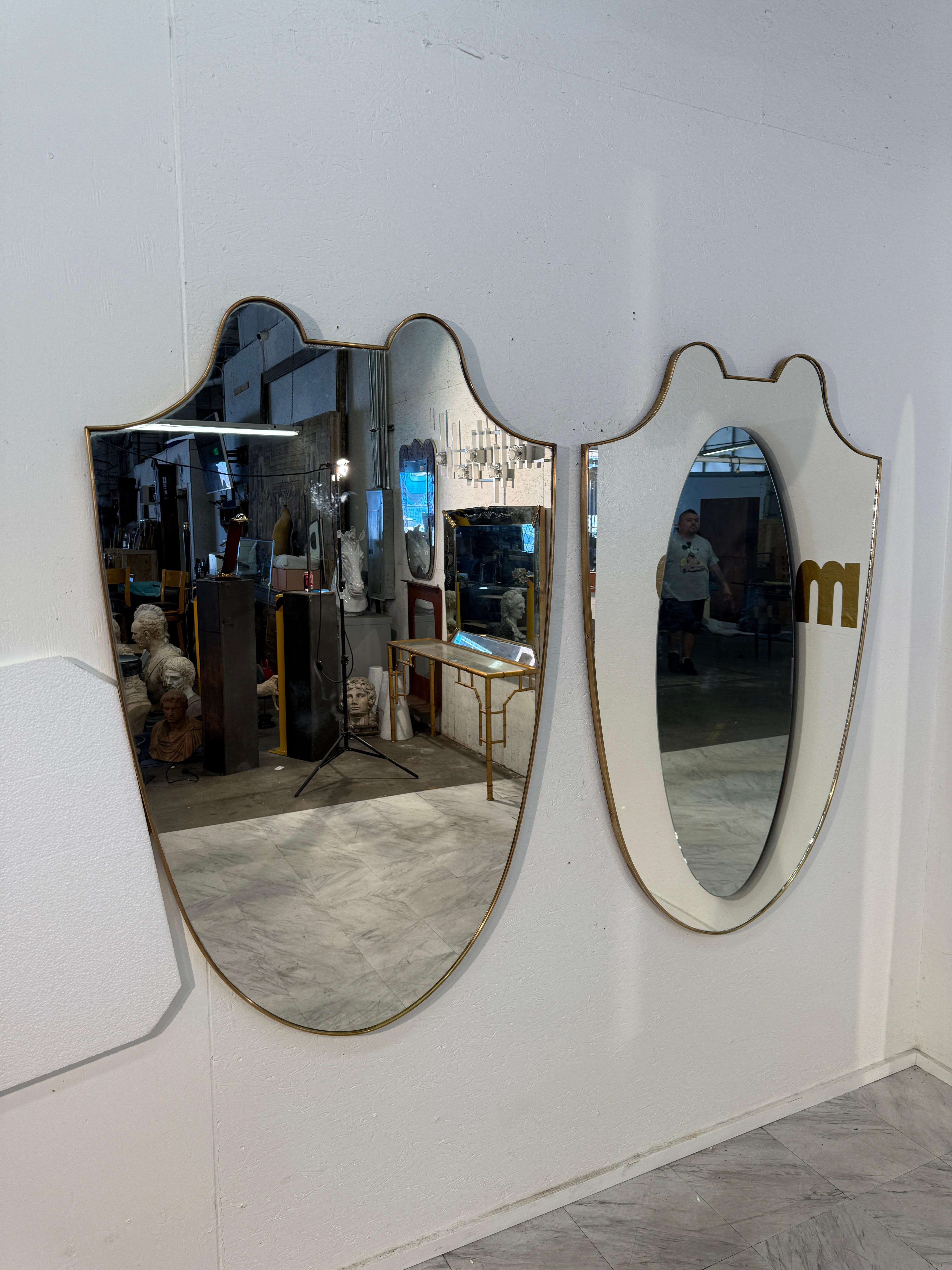 Una raffinata coppia di specchi da parete italiani degli anni '50, ognuno dei quali è caratterizzato da una graziosa silhouette a forma di scudo incorniciata in ottone. Le loro forme curvilinee, con contorni fluidi e picchi morbidi, riflettono