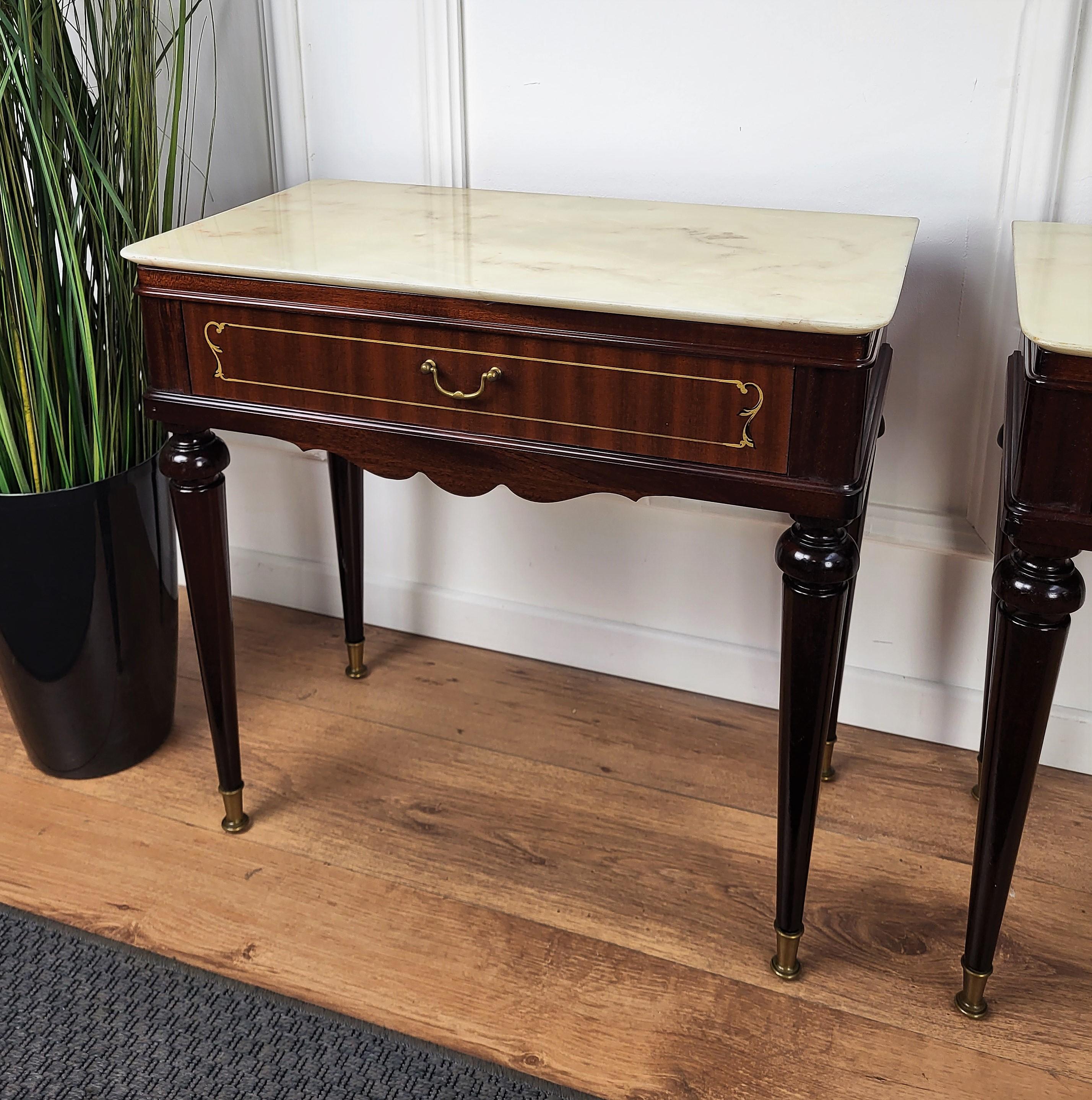 Very elegant and refined Italian 1950s neoclassical pair of night stands bed side tables with greatly carved detailed and decorated wooden structure, wood veneer decorated front drawer and white marble top with brass details and fluted reeded legs.