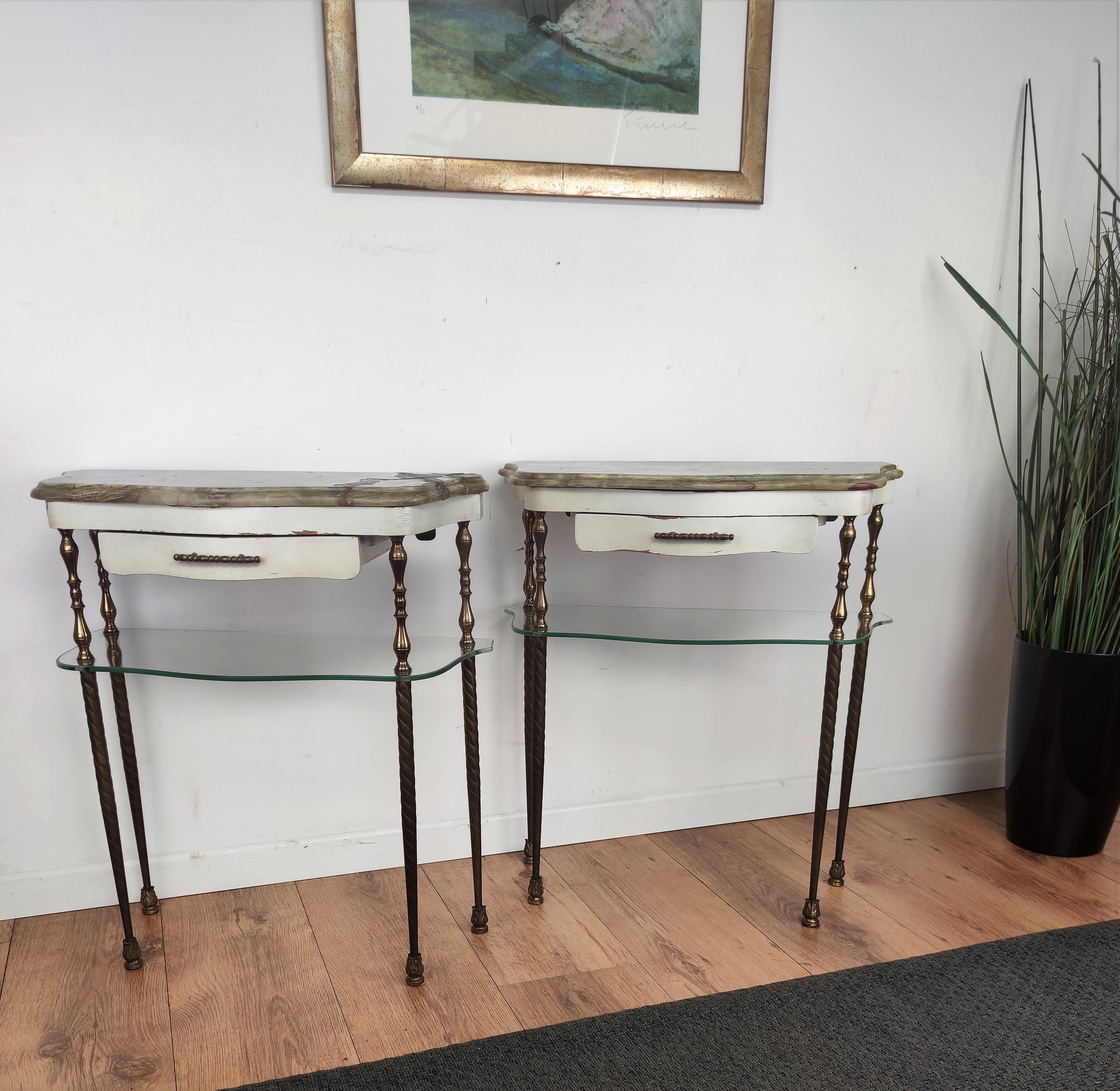 Very elegant and refined Italian 1950s neoclassical pair of bed side or end tables with 2 tier gren marble top, wooden drawer and glass shelf standing on 4 beatifully and detailed side brass decorated legs or structure. Those side tables or