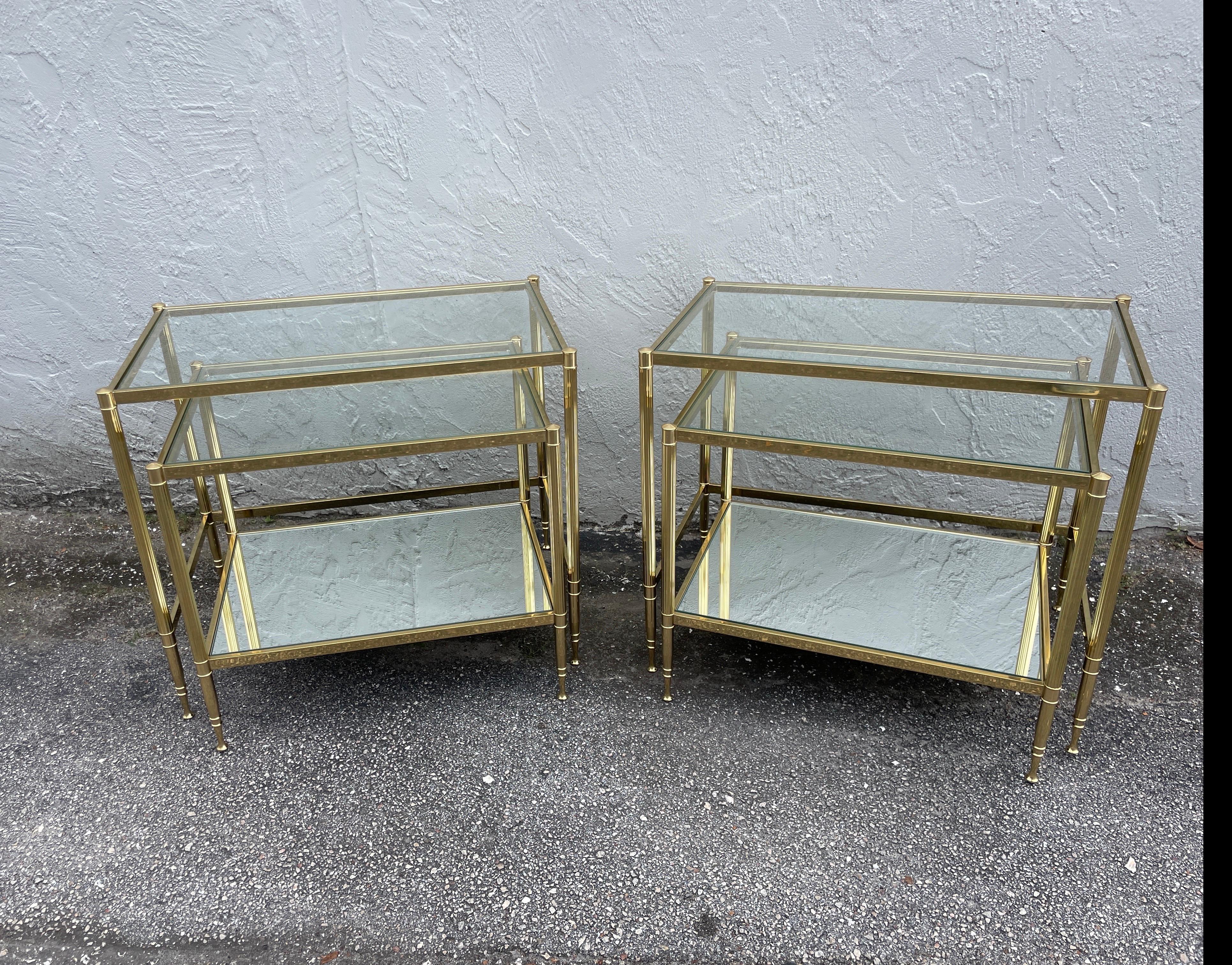 Vintage Paar Beistelltische aus Messing im neoklassischen Stil von Maison Bagues. Der obere Tisch hat eine Glasplatte und der kleinere untere Tisch hat eine Glasplatte und eine untere verspiegelte Ablage.
Der kleinere Tisch ist 15,25