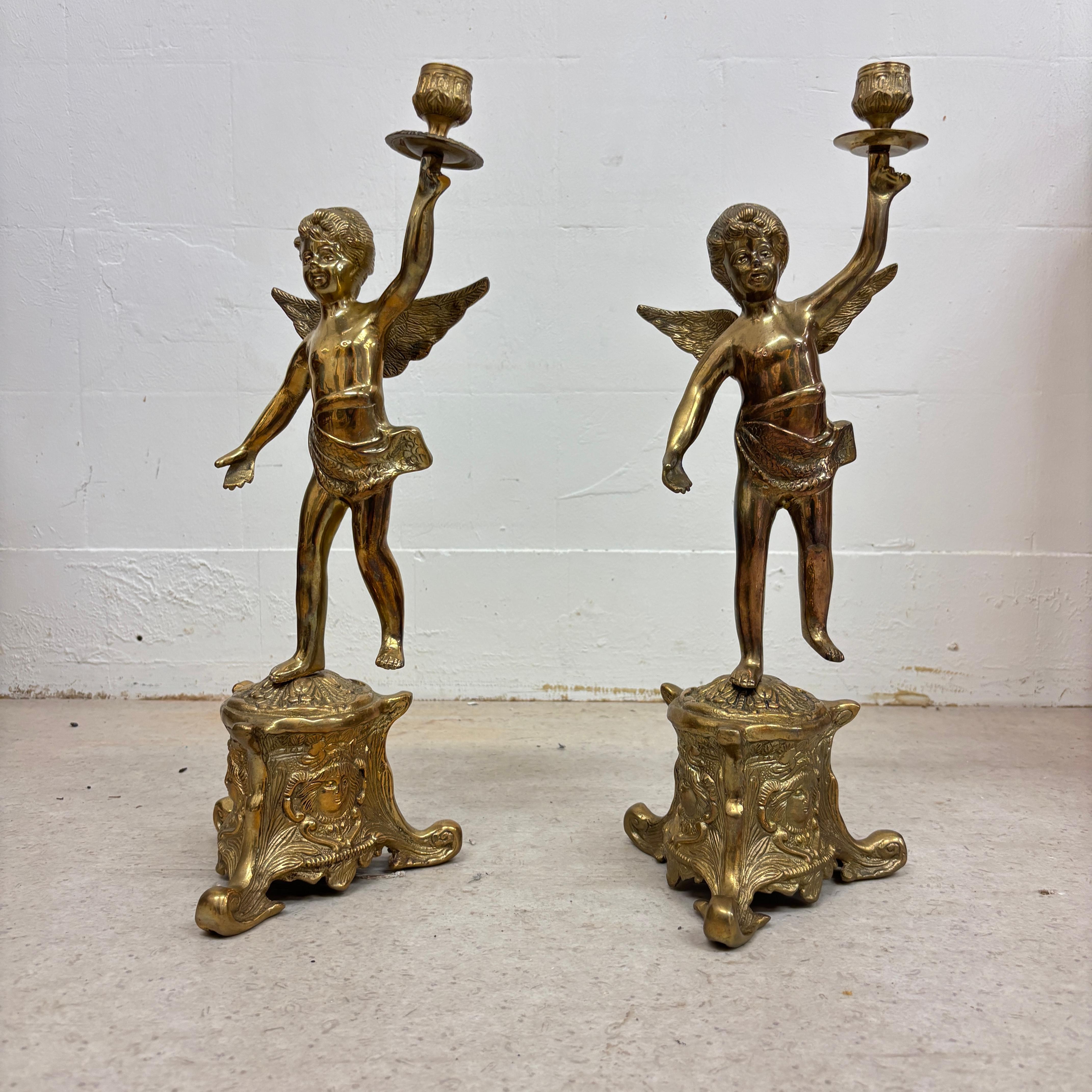 Paire de bougeoirs élégants et magnifiquement détaillés en bronze italien représentant des chérubins ailés dans des poses dynamiques et pleines d'entrain. Chaque figurine repose gracieusement sur une base sculpturale ornée de motifs classiques. Les