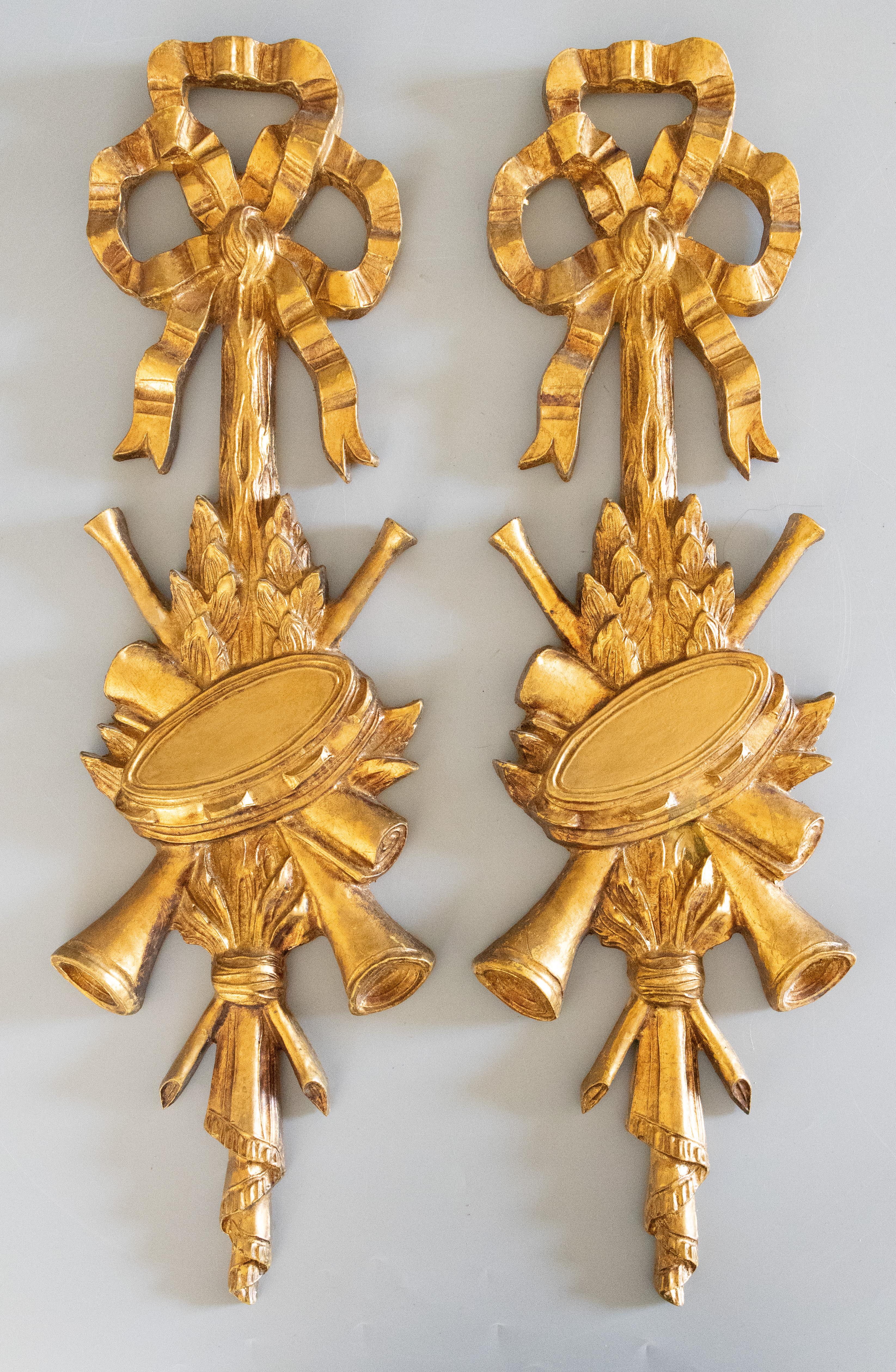 A gorgeous pair of Mid-Century Neoclassical Italian carved gilt wood musical instruments wall garland / accents / ornaments. These fabulous wall hangings have carved bows, tambourines, horns, and laurel garland in a beautiful gilt patina and would