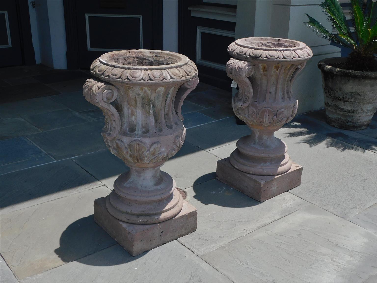 Pair of Italian hand carved sandstone fluted campana form garden urns with flanking egg & dart borders, acanthus scrolled handles, and resting on circular squared plinths. Early 19th Century. 23.5 wide at arms, 19.5 diameter top , 15.5 squared base. 