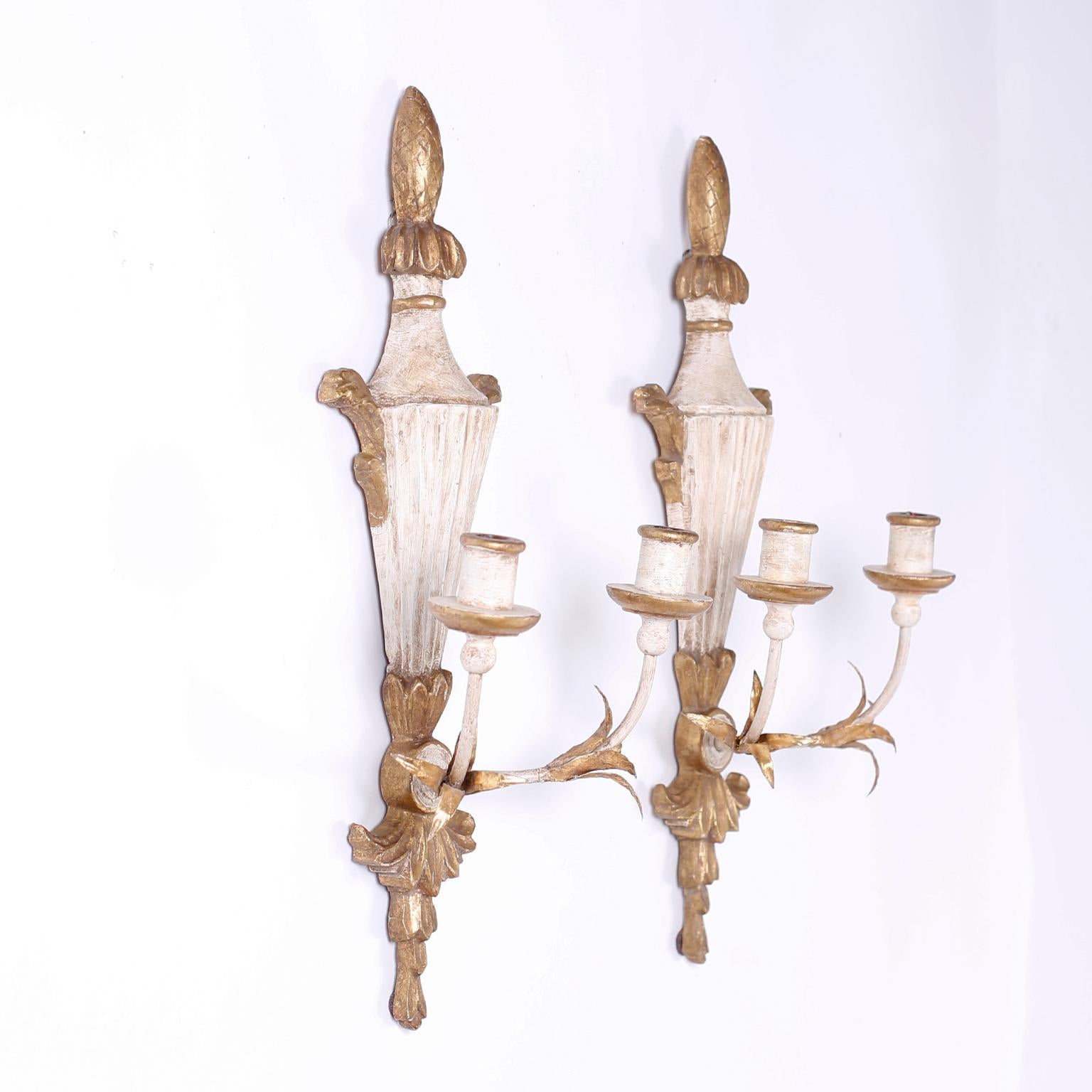Pair of antique two-light carved wood Italian wall sconces with classical form, distressed white paint, metal arms, and gilt highlights.