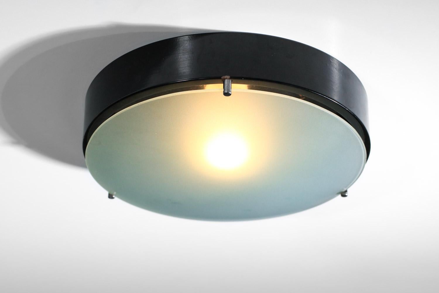 Pair of Italian ceiling lights from the 60s by Stilnovo. Round structure in black lacquered metal and large opaque glass lens. Can be used as wall lights (see photos). Beautiful vintage condition, with traces of oxidation on the metal parts. One E14