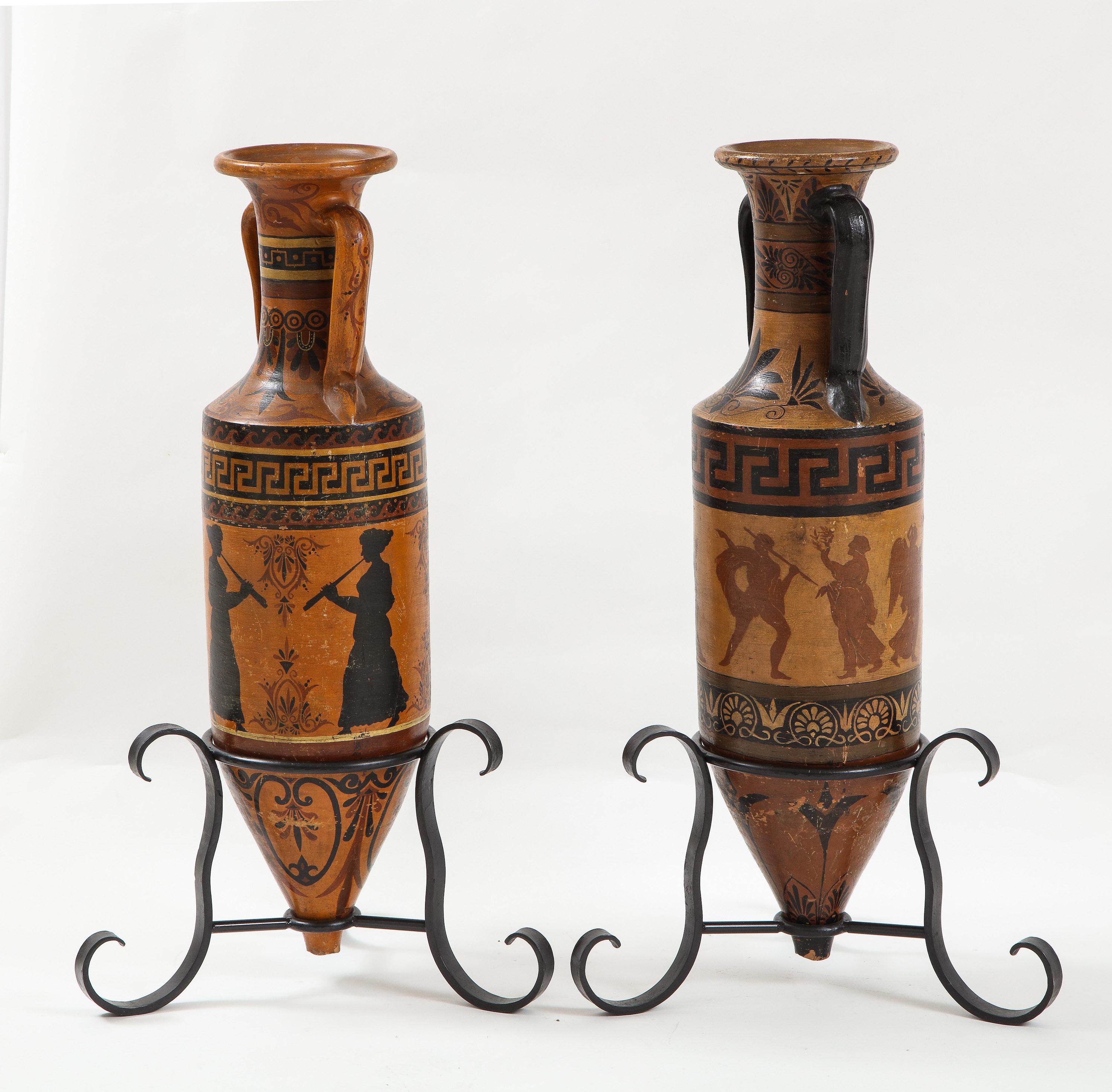 Pair of Italian ceramic amphora’s in the Etruscan style with painted neoclassical figures. Set on later iron bases.