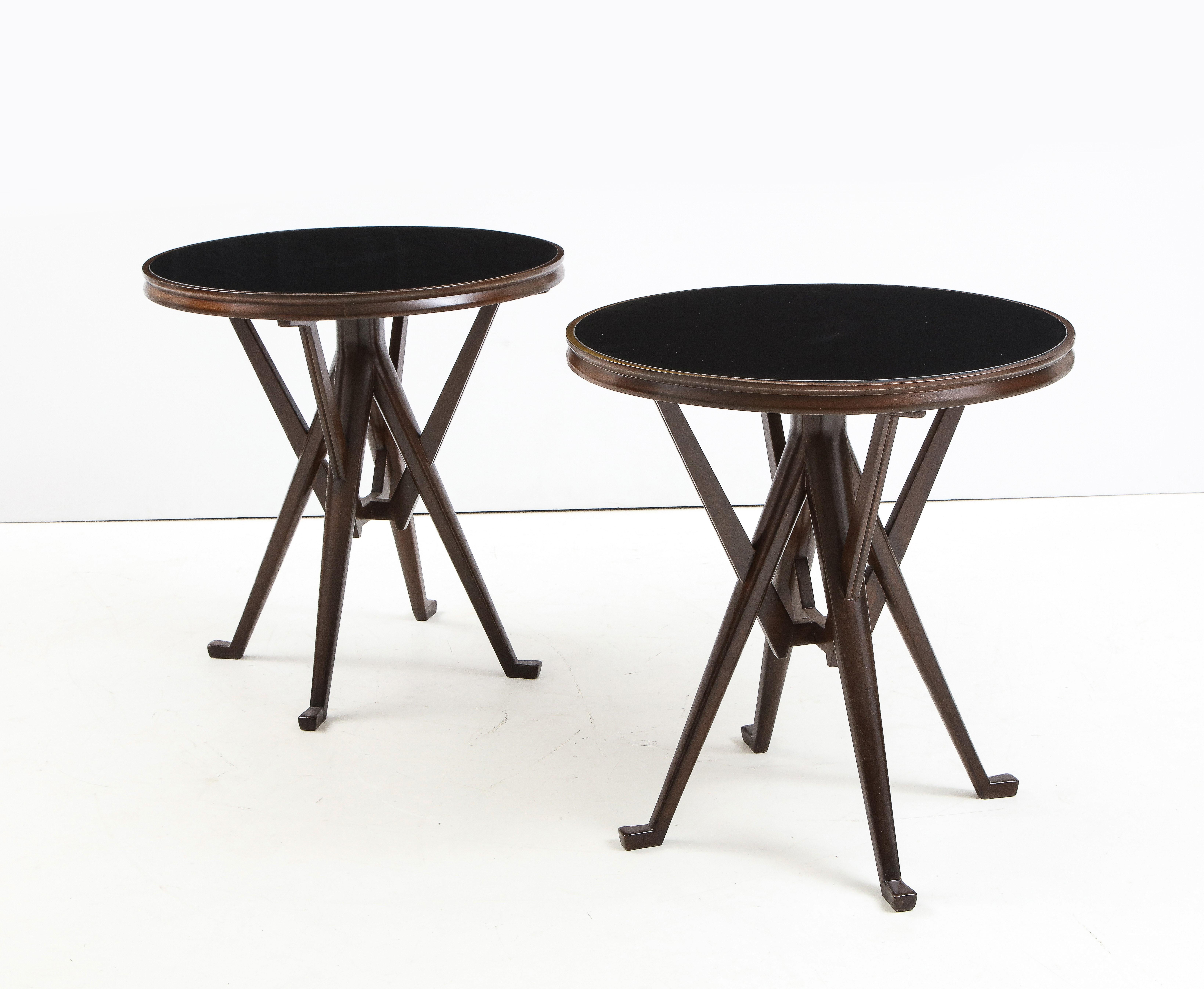 A pair of sculptural Italian mid-century dark brown circular side tables attributed to Ico Parisi with black painted glass inset tops resting on a solid wood frame with four legs with splayed feet, joined into a single short central support