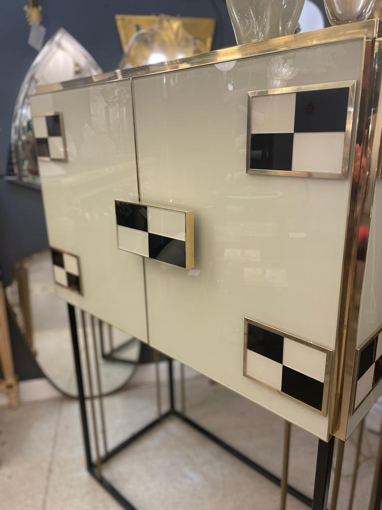 An elegant pair of Italian Dry Bar fitted with brass hinges and solid legs, wood interior with shelves. The cocktail cabinet is completely adorned by finish Venetian glass with rectangular decorations in ivory&black. Italy, circa 2000s.