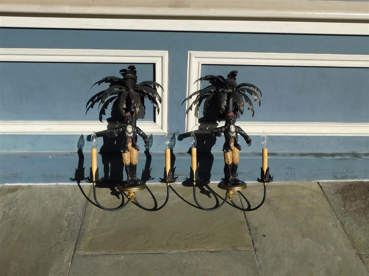 Pair of Italian cold painted tin and iron figurative dancing monkey wall sconces with flanking decorative palm trees, two scrolled foliage candle arms, and circular gilt plinths with foliage ball finials, 20th Century  Pair of wall sconces have been