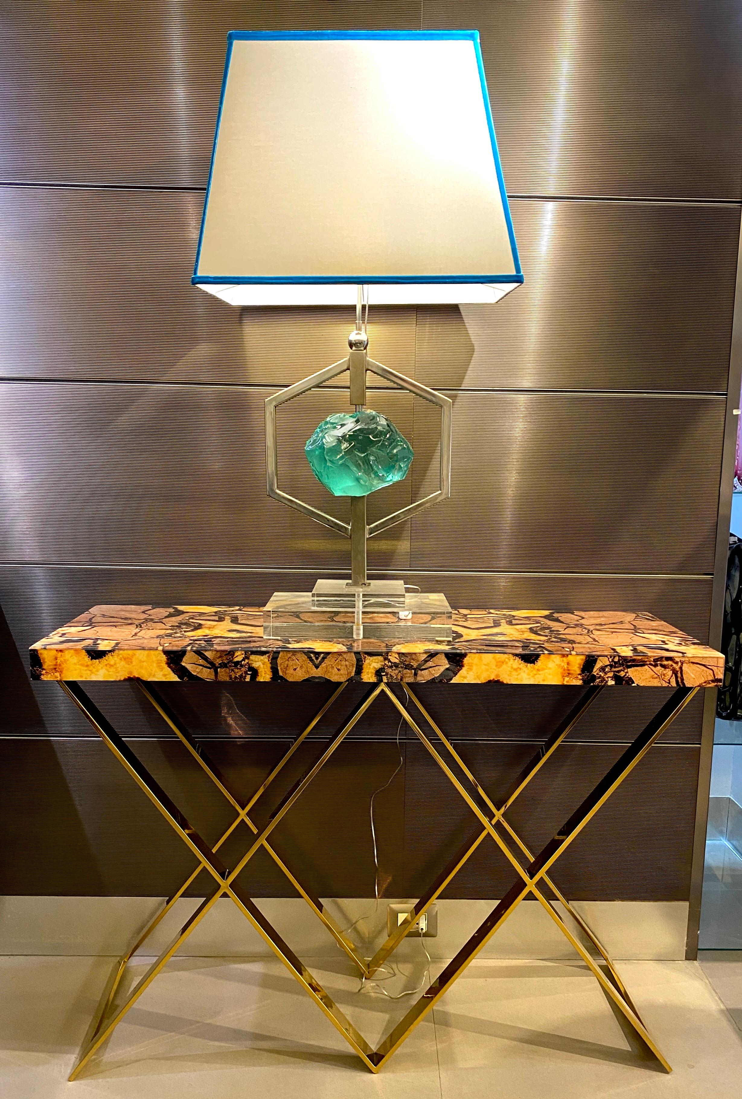 Exceptional console Tables with double X-shaped brass base .
The glass tops of these pair of consoles are made with the imitation of a semi-precious stone called “septaria”, which is formed by overlapping mineral deposits and is crossed by crystal