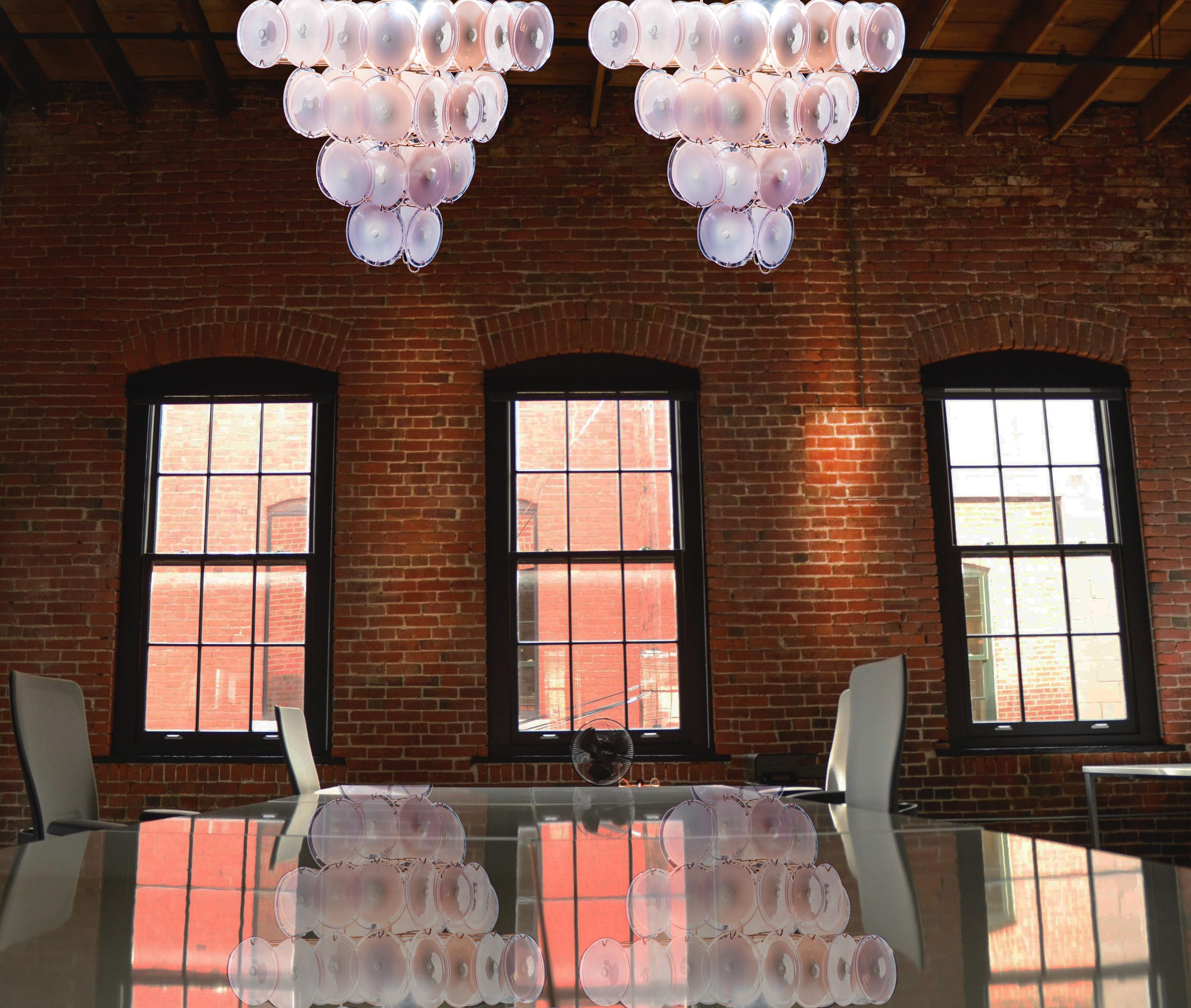 Each chandelier is made of 52 pink discs of precious Murano glass are arranged on four levels. Nine lights.
