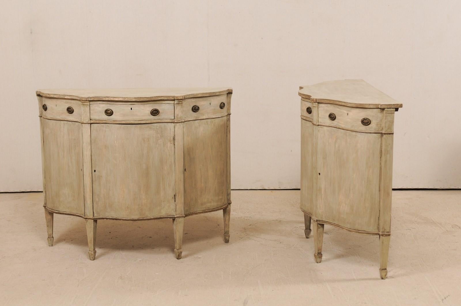 A pair of Italian demilune painted wood console chests from the early 20th century. These antique Italian demilune cabinets each feature beautifully scalloped tops over a serpentine cabinet base which fluid design mimics the shape of it's top. There