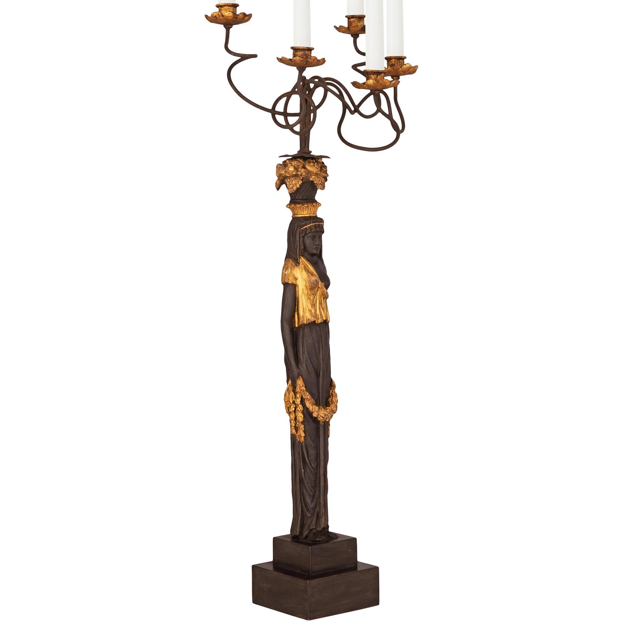 A unique and very decorative pair of Italian 19th century Neo-Classical st. ebonized Fruitwood, giltwood, and gilt metal candelabras. Each five arm candelabra is raised by a stepped square base where the beautiful Egyptian maidens are standing. Each