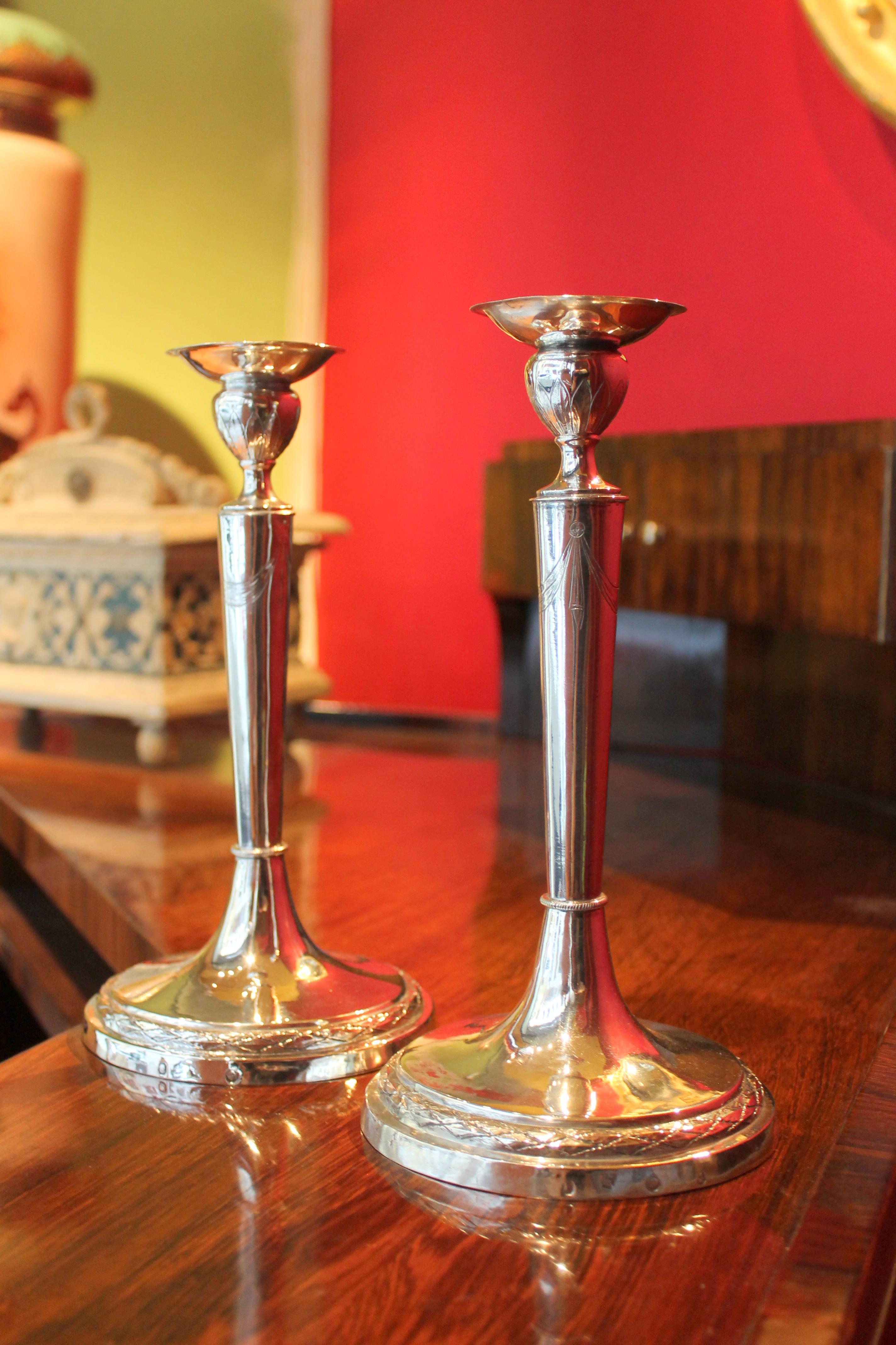 This pair of elegant 19th century Italian Empire period (1811-1817) silver chiseled candlesticks show a simple but elegant design and shape. 
The conical structure embellished with festoon and garlands rests on an unfilled round base decorated with