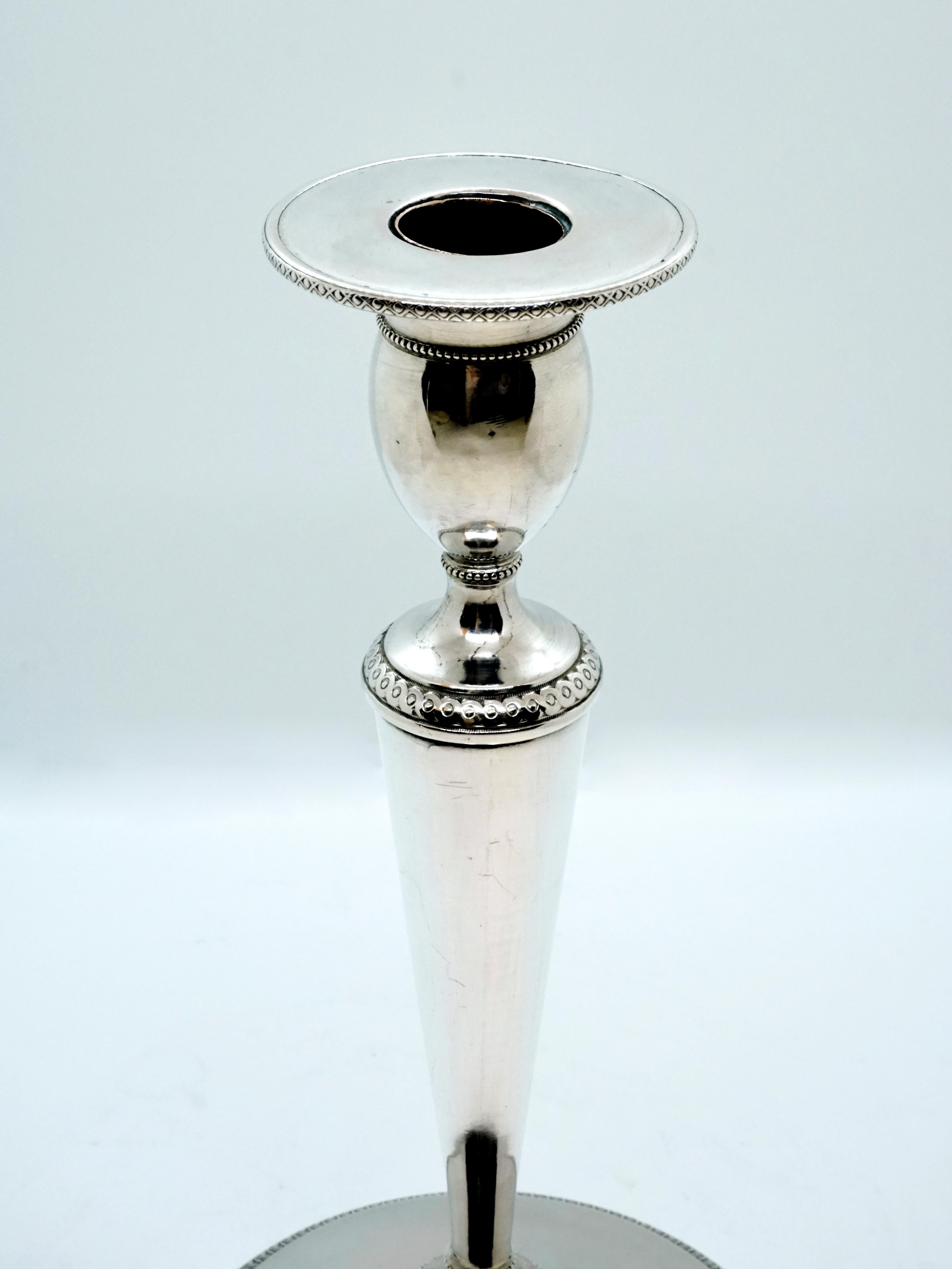 Pareja de elegantes candelabros Imperio sobre base sin relleno, estructura cónica, ojales desplazados en forma de oliva con borde de goterón plano en forma de plato, diseño liso y sencillo de la superficie dividida por delicados frisos de hojas y
