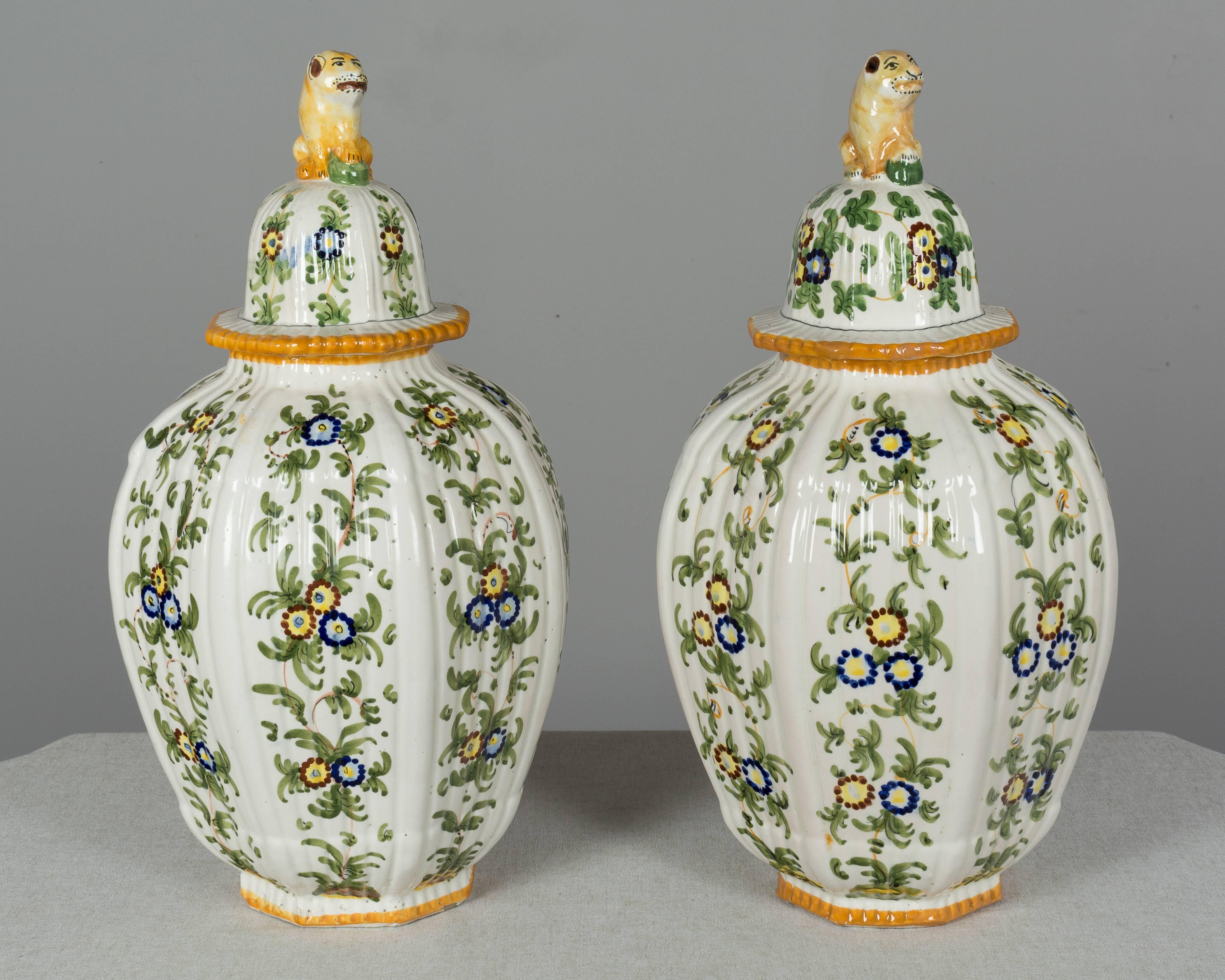 A pair of Italian faience ginger jars with traditional ribbed urn form and lids topped with foo lion knobs. Each with hand painted floral decoration in green with yellow trim. The lion on one of the lids was broken has been professionally restored.