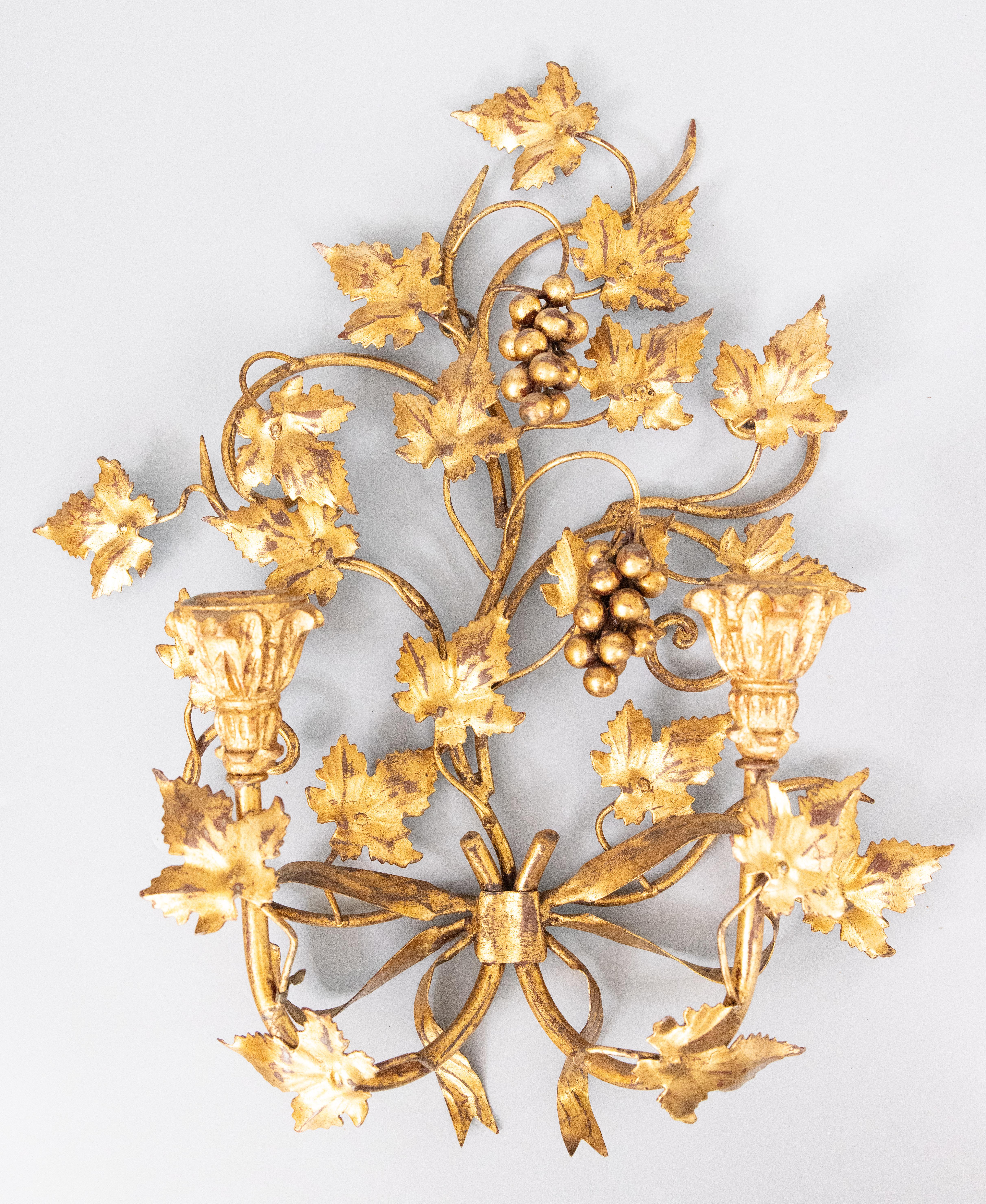 A gorgeous vintage pair of Italian Florentine gilt tole two-arm candle sconces with lovely grapes, scrolling leaves, large bows, and carved giltwood candle holders, circa 1950. 