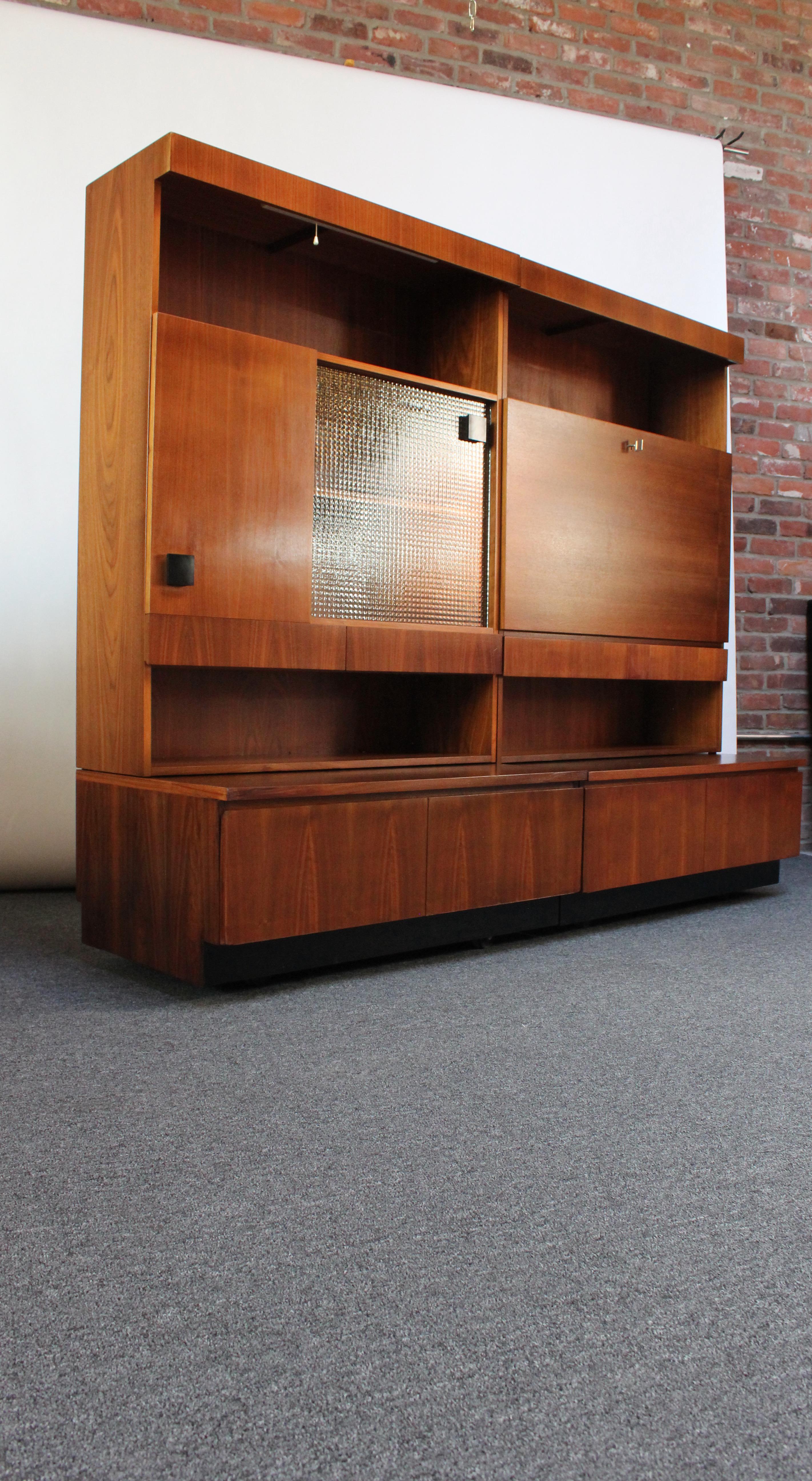 Stylish freestanding wall units boasting bookmatched walnut veneer (ca. early 1970s, Italy). Each comes with a black vinyl seat (more for decoration than practical use).
The first unit features a functional light with elegant pull on / off string