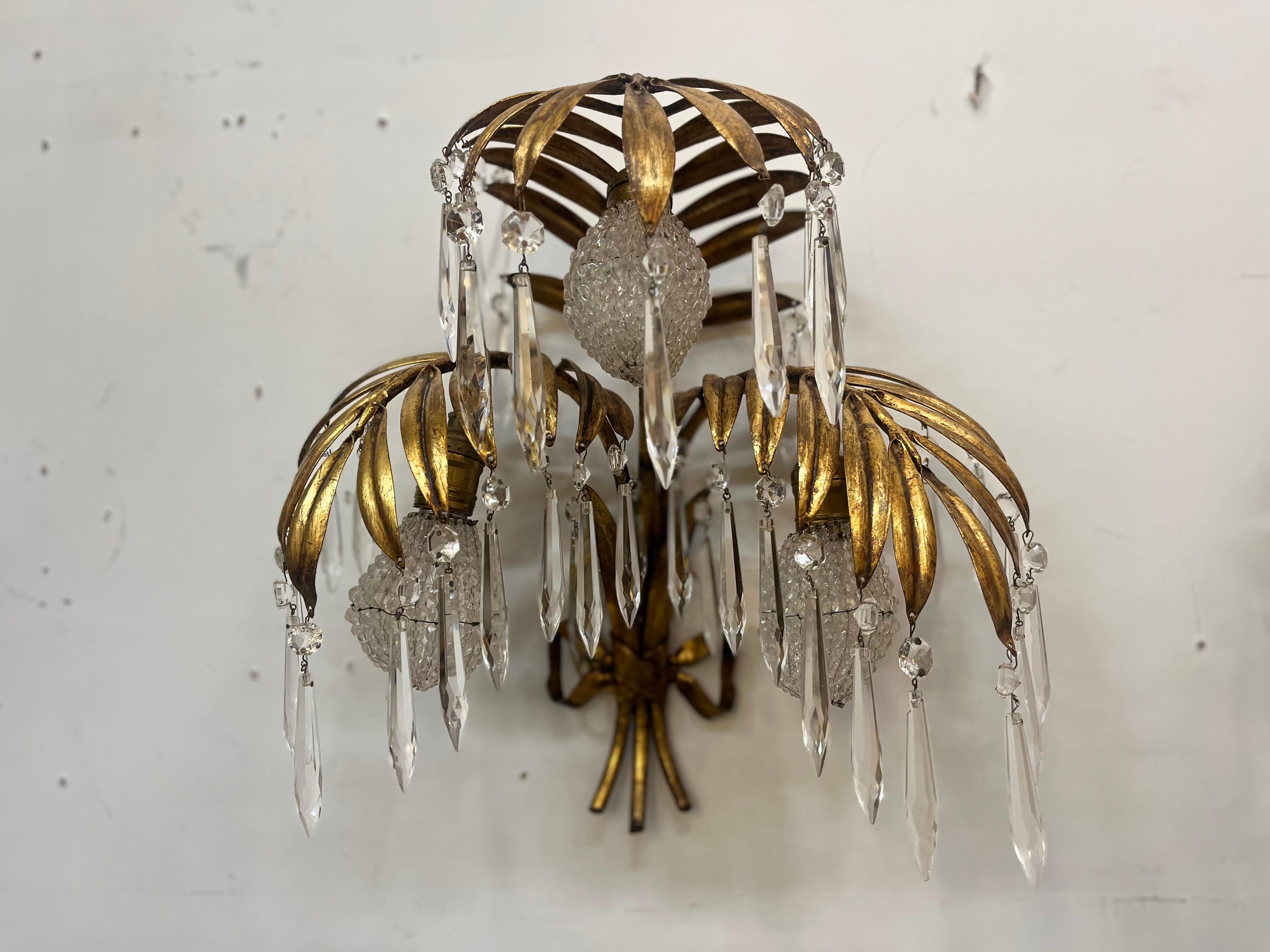 Coppia di applique italiane. Fondo a tre palme in metallo con lavaggio dorato. I bulbi sono ricoperti da sfumature di perline e le alette sono allungate da prismi di cristallo. Il tutto legato da un fiocco di metallo. Ricablato e pronto per essere