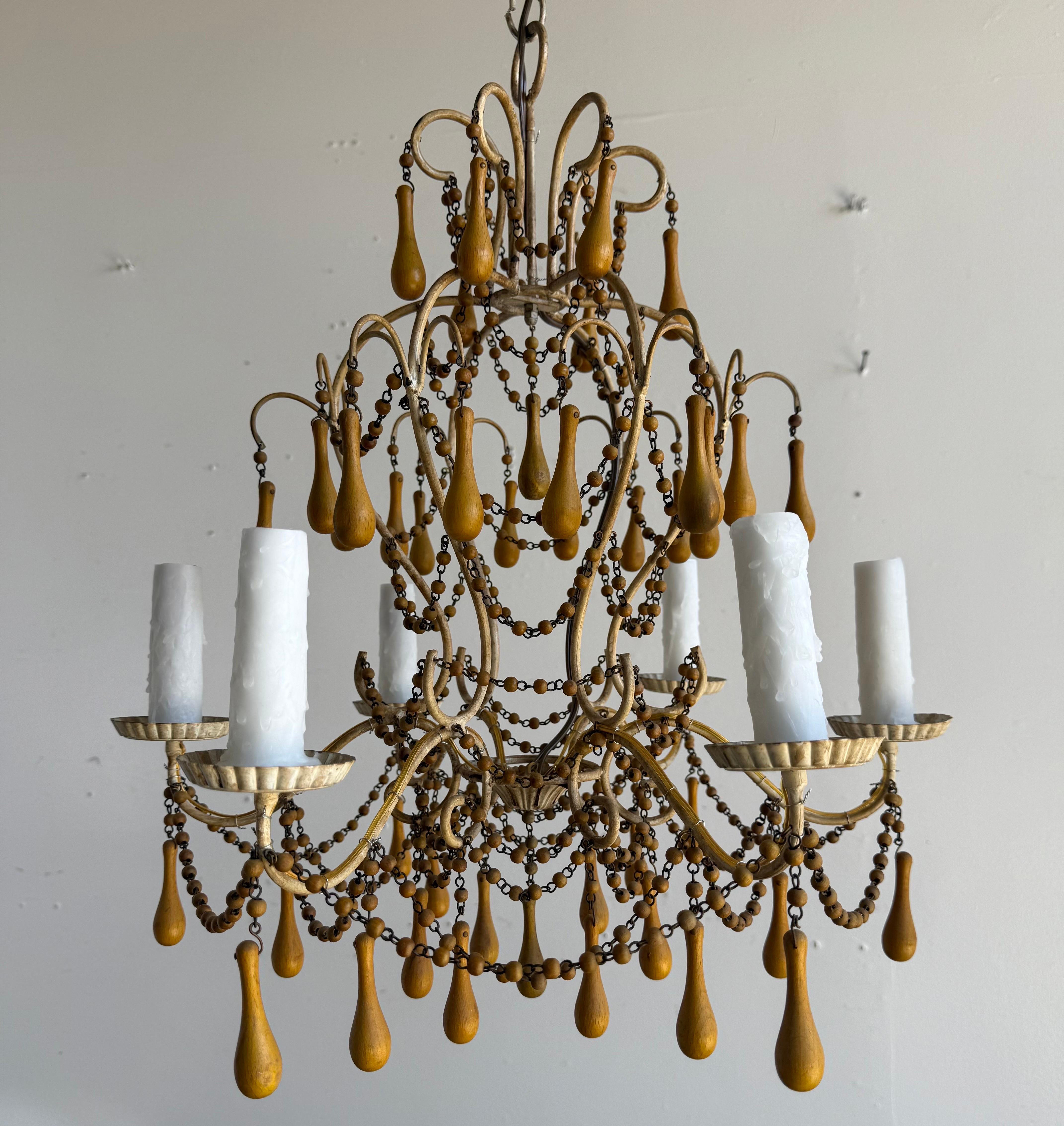 A graceful pair of Italian chandeliers in gilt iron, dating to the mid-20th century, distinguished by their elegant form and unusual ornamentation. Each chandelier features six candle-form lights with scalloped bobeches, arranged around a scrolling