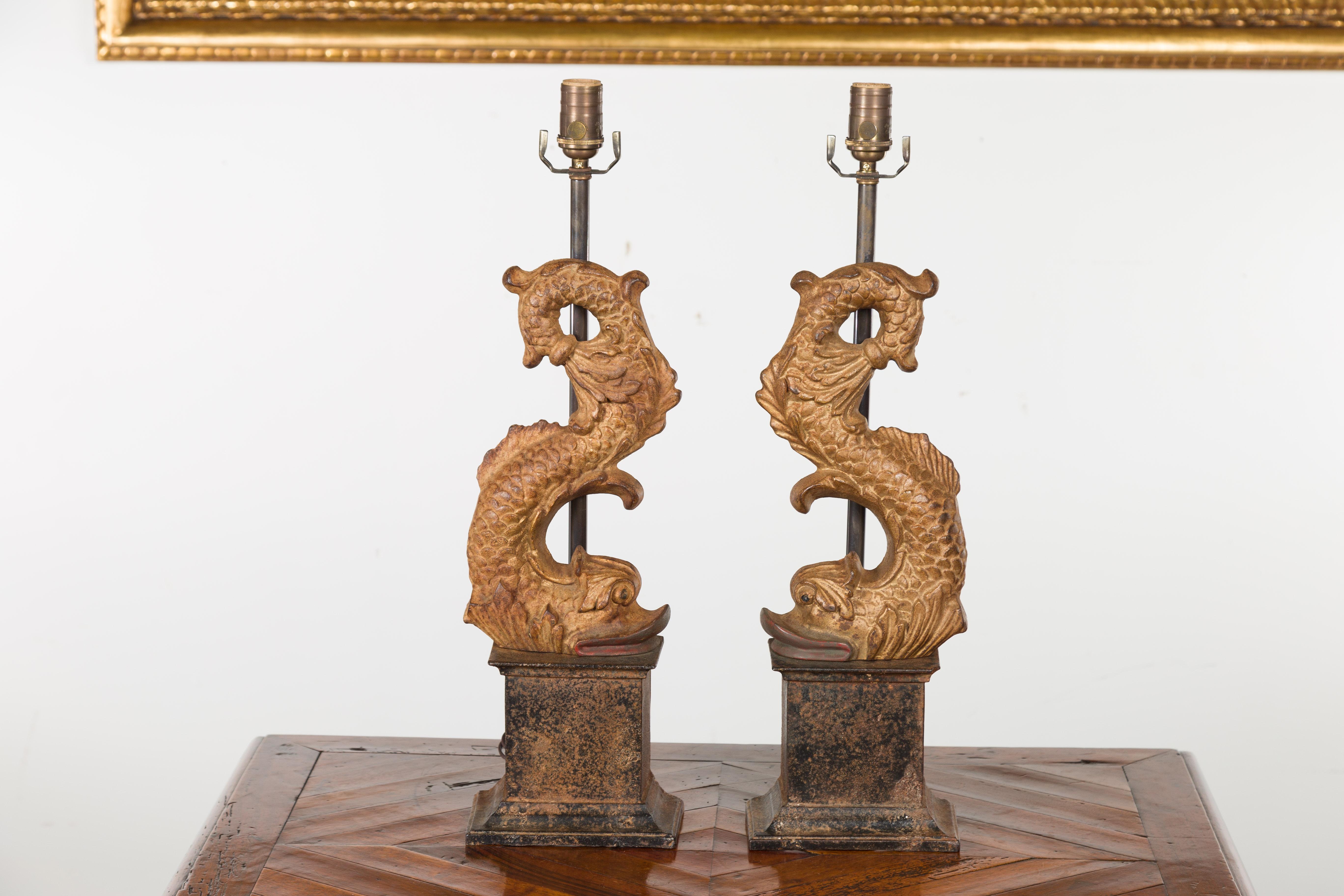 A pair of Italian gilt iron Baroque style dolphin sculptures from the early 20th century, made into lamps and mounted on tall bases. Created in Italy during the first quarter of the 20th century, each of this pair of sculptures features a dolphin