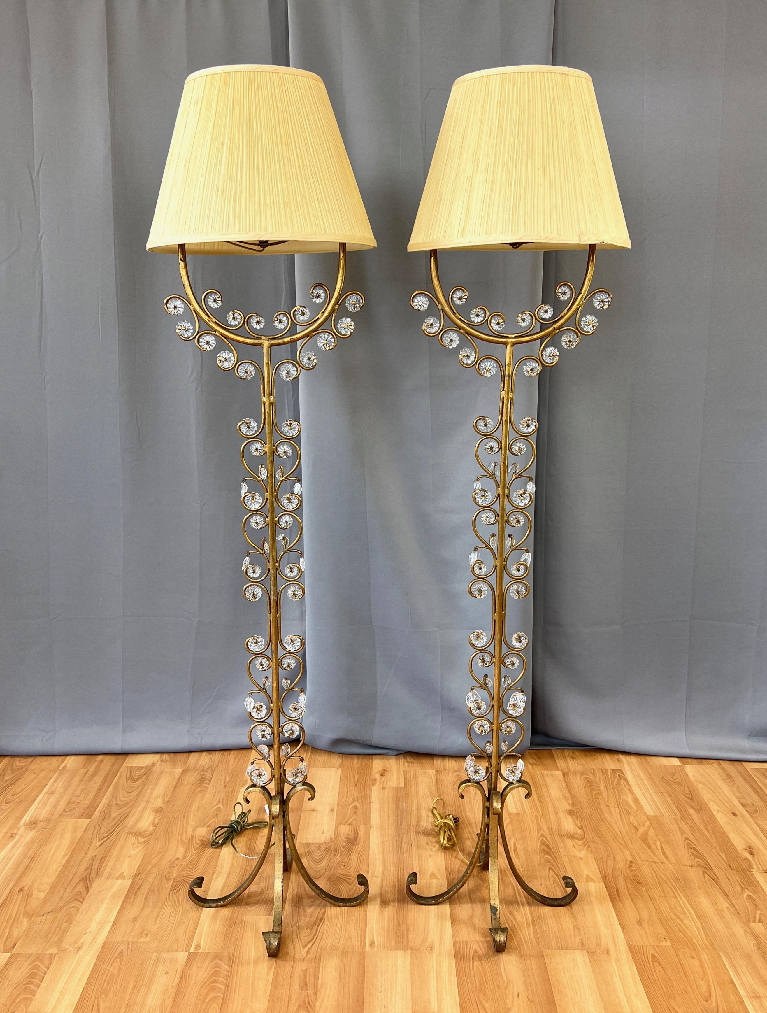 An enchanting pair of tall 1950s Italian gilt wrought iron floor lamps with glass floret & leaf adornments. 

Hollywood Regency heavy wrought iron form with gilt-style finish features elegant scroll work from top to bottom. More than six dozen