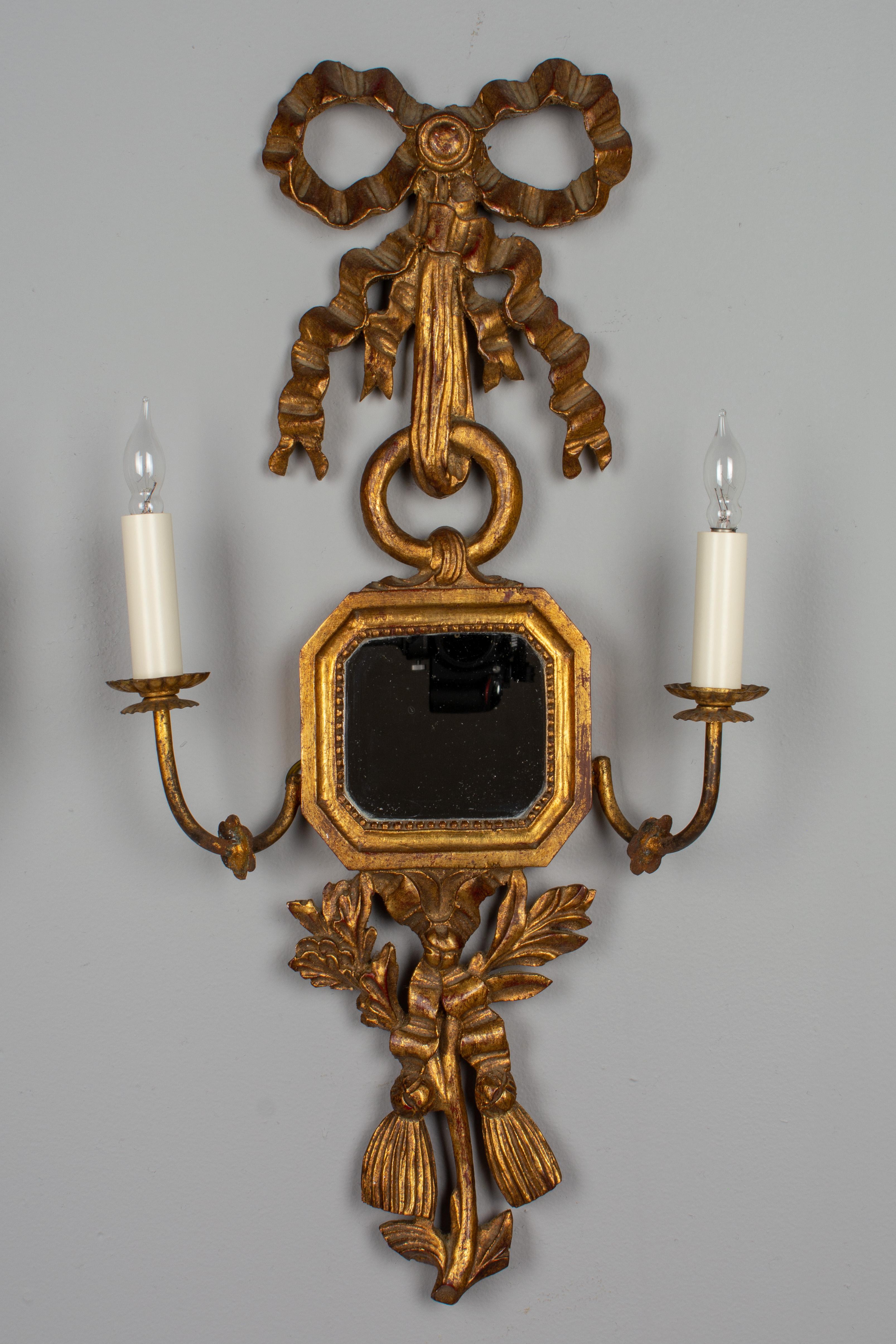 A pair of Italian Palladio style gilded wood two-light candle sconces with framed mirrors. Carved with ribbons, swags, and tassels with warm gilt finish. Each with two gilded metal candle arms. Electrified with new sockets and a ground wire will