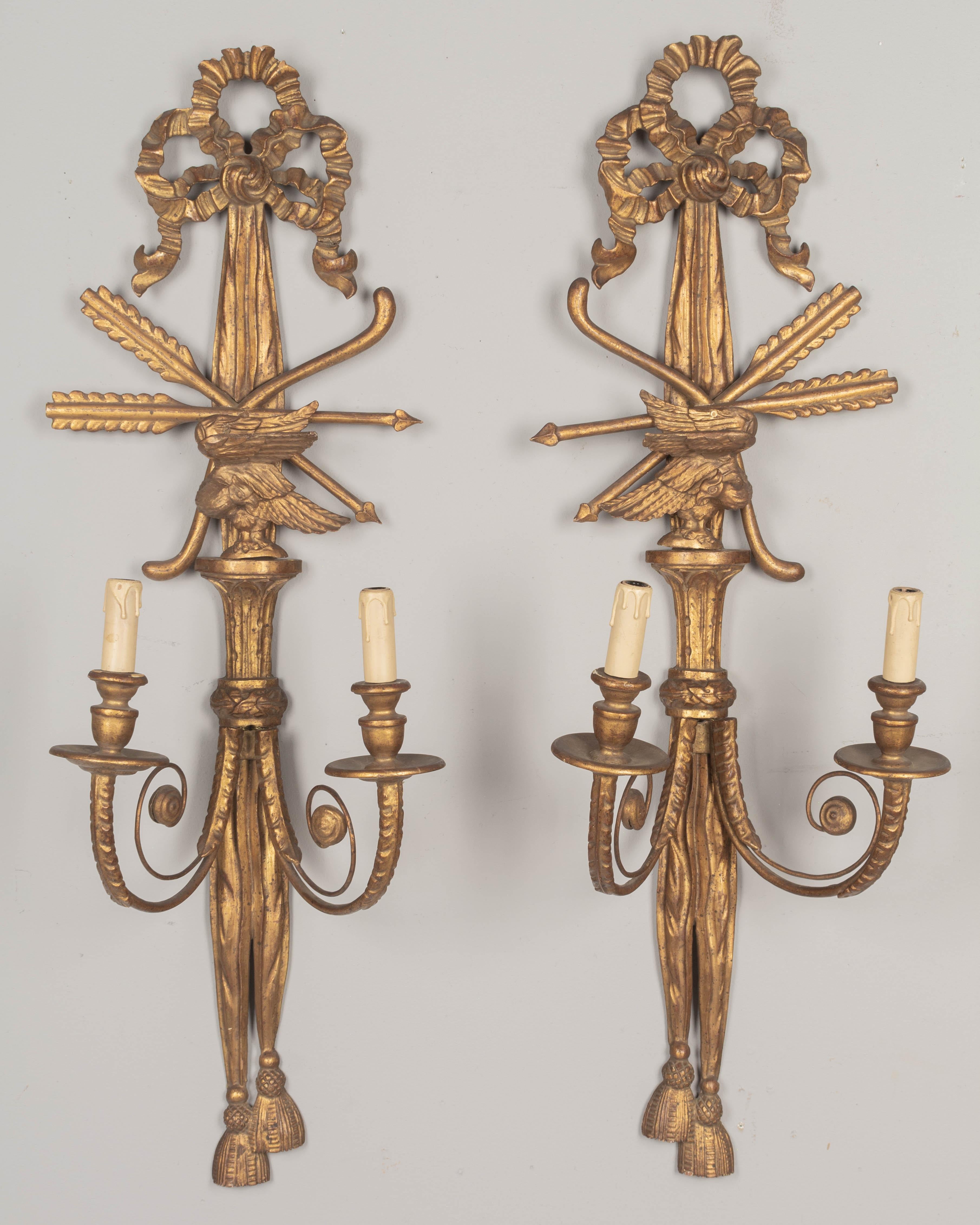 Paire d'appliques italiennes à deux lumières en bois doré, chacune avec des glands et des rubans drapés sculptés, et un oiseau en trois dimensions. En bon état, avec une chaude patine dorée. Deux bras de bougie en métal à enroulement avec détails de