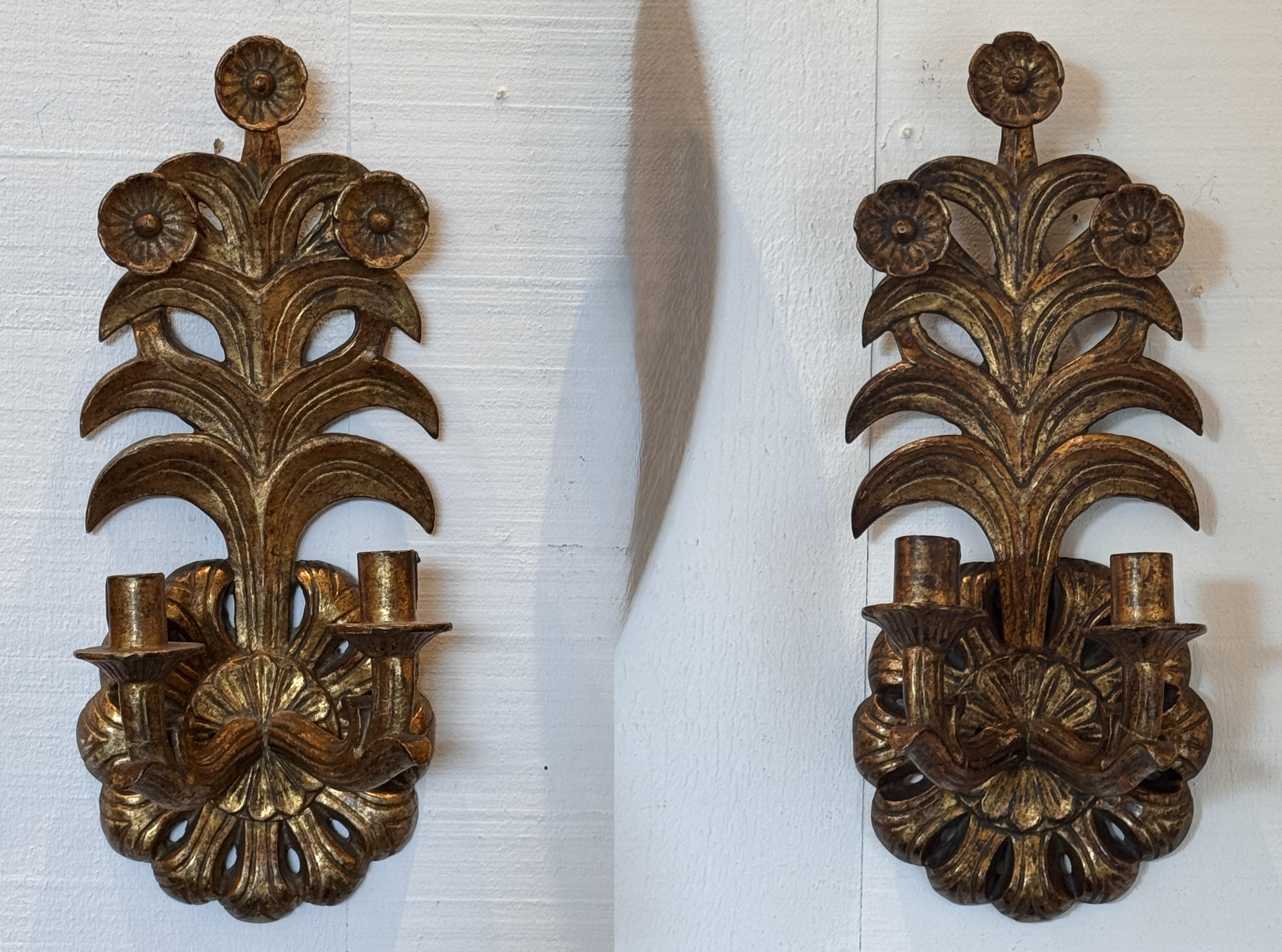 Paire d'appliques italiennes en bois doré, chacune sculptée d'un motif floral et feuillu stylisé. La forme à deux bras est finie dans une riche surface dorée avec une patine vieillie, mettant en valeur les détails sculptés.