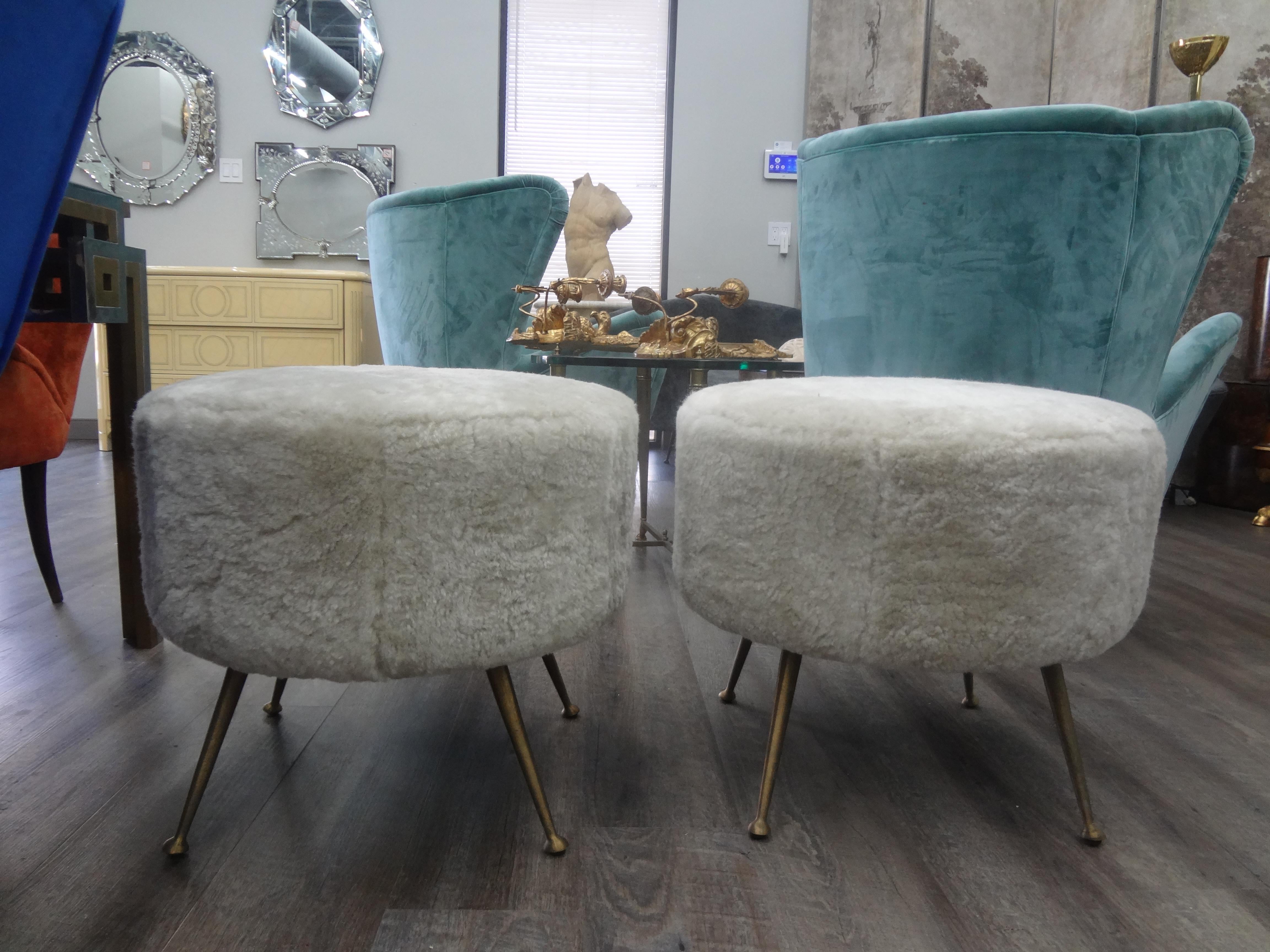 Great sculptural pair of Italian Gio Ponti inspired round poufs, ottomans, stools or benches. This stunning pair of vintage Italian midcentury ottomans with splayed brass legs are newly upholstered in plush cream colored sheepskin. Perfect where