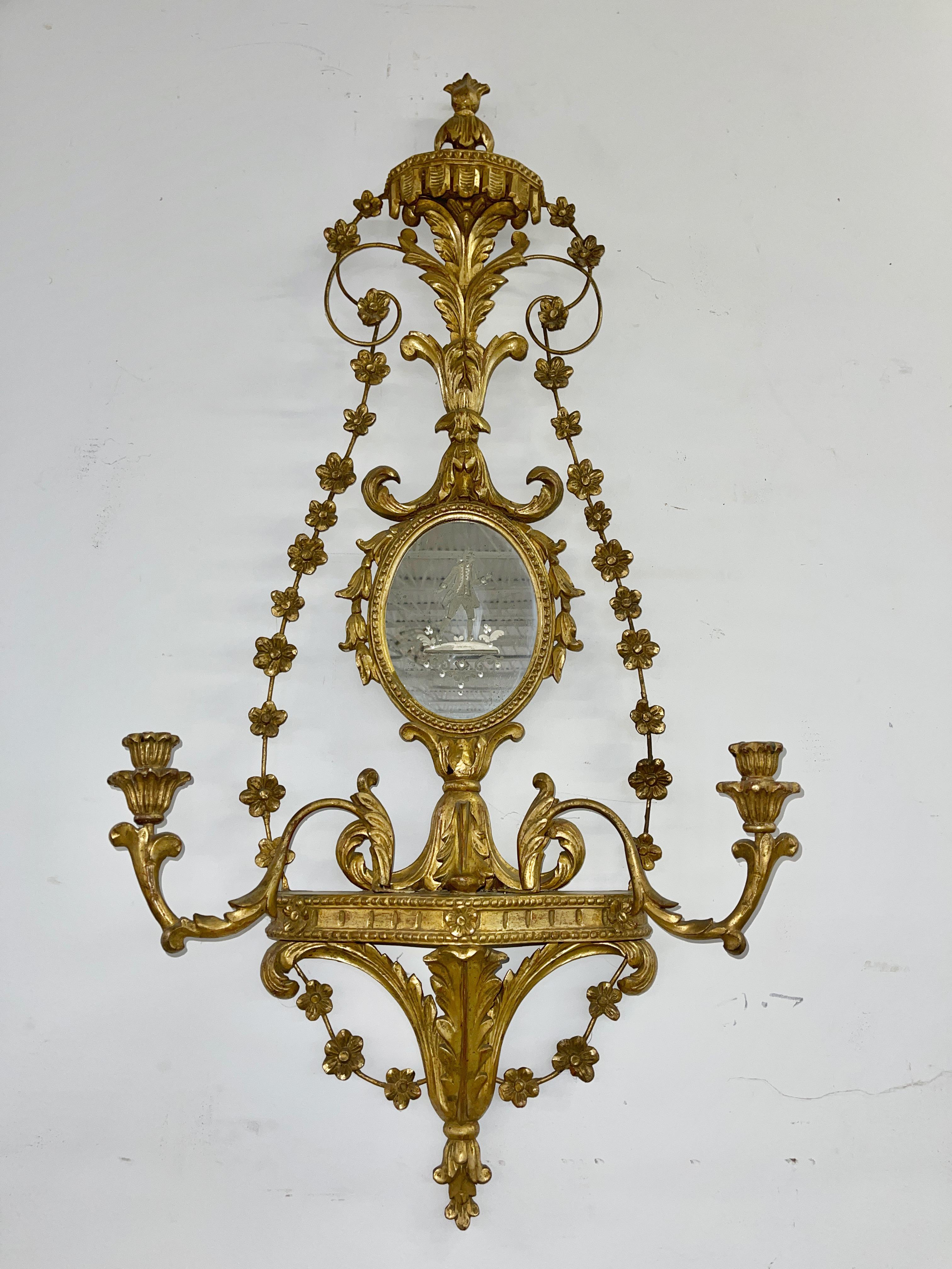 Very elaborate scrolling foliate carvings on these Italian giltwood girondole mirrors with candle sconces. 
Oval mirrors reverse etched with Venetian figures, male and female. 
Candle holder arms are positionable. 
Very fine condition with no