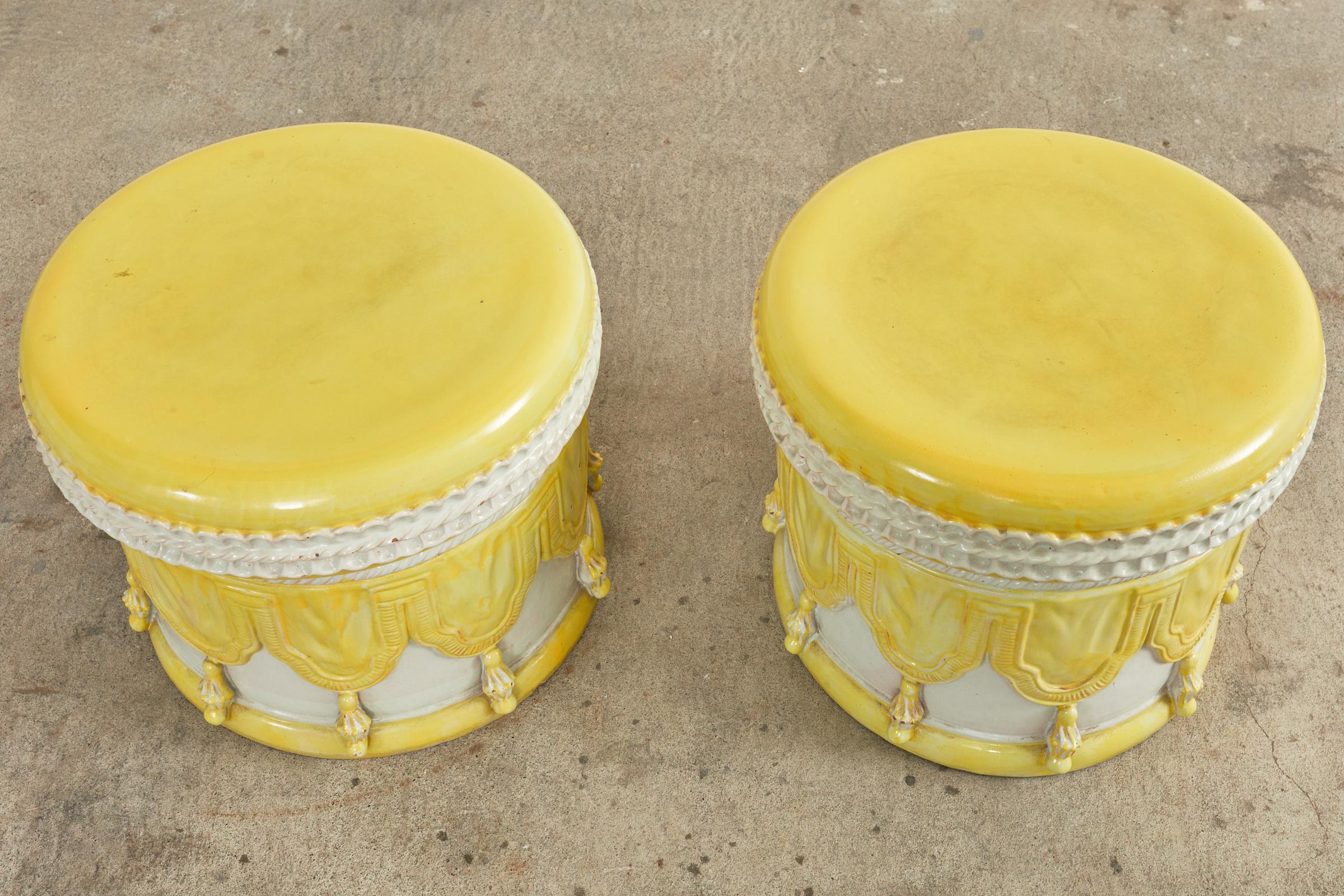 Whimsical pair of Italian regency glazed ceramic garden stools or drinks table. The matched pair feature trompe l'oeil swag with tassels on the sides of the drum form bodies. Beautifully finished in a citron yellow with white. The tops resemble