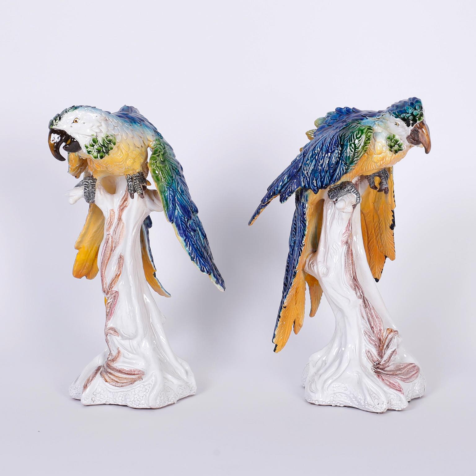 Pair of Italian glazed terra cotta parrots or birds composed with animated expressions, decorated with lush tropical colors, and perched on tree trunks. Signed made in Italy on the bottoms.