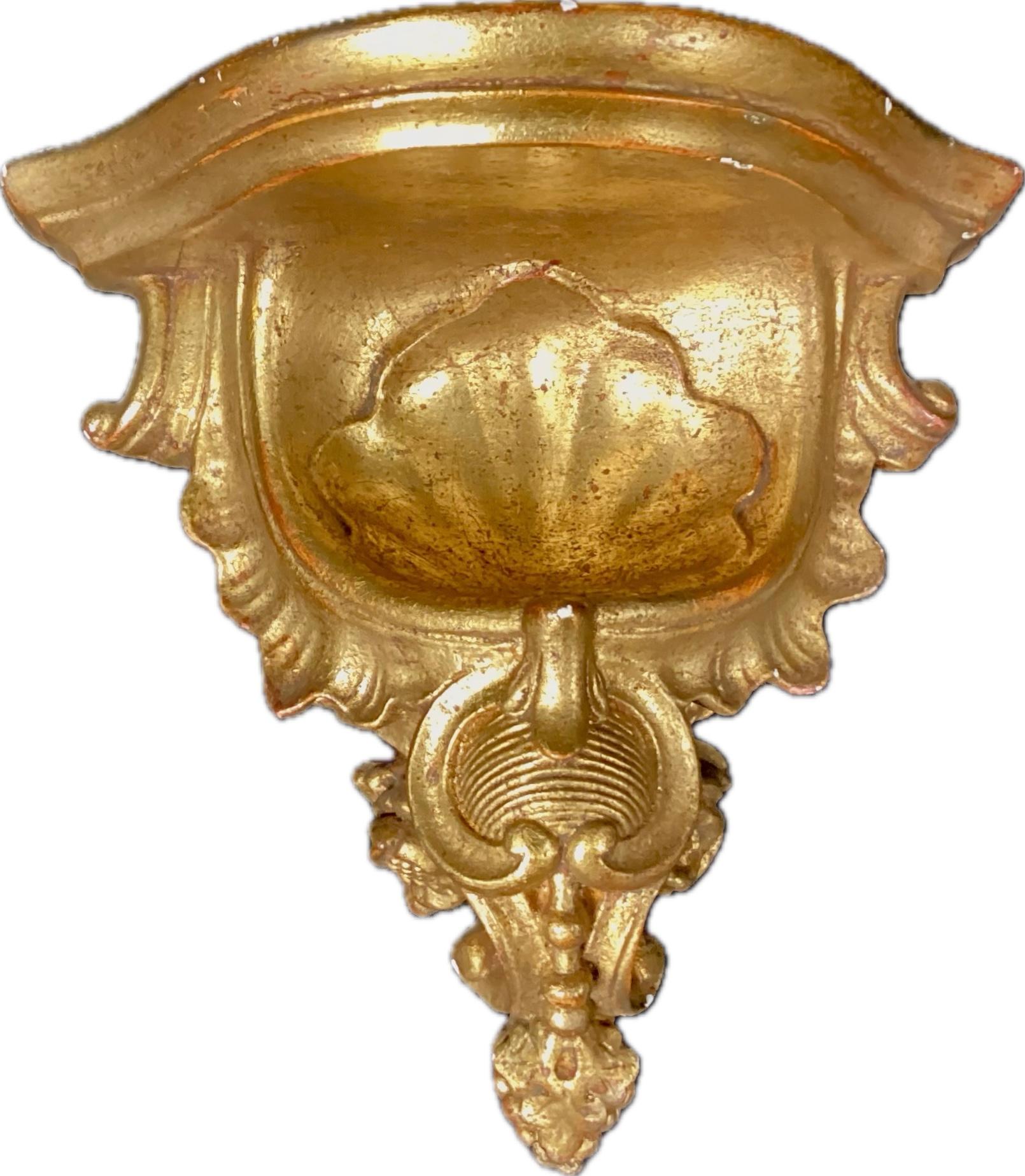 A Pair of Italian Rococo Style Gold Gilt Wall Brackets. Brackets feature impressive gold scrolling with floral motif. Top of shelf is painted black. Hangers in place on reverse side. Wonderful patina throughout.