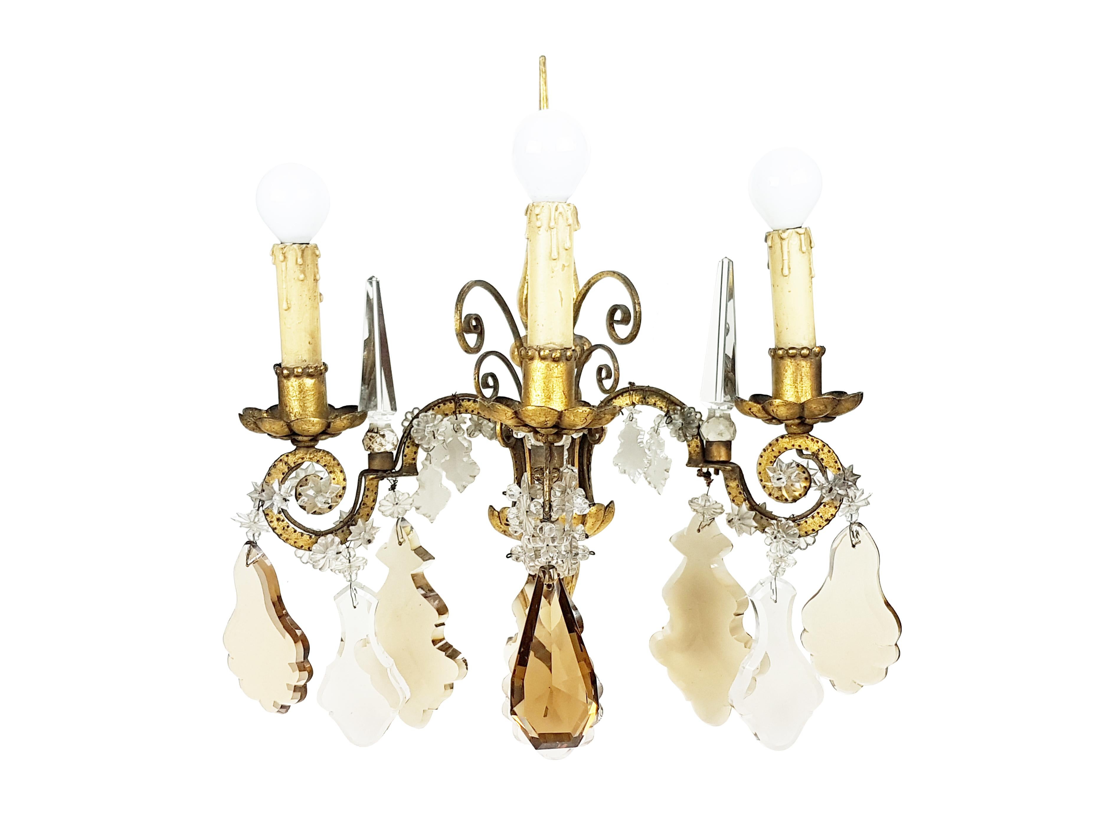 This pair of wall lamps was produced in Italy in the 1930s. It consists of a golden leaf metal structure with different faceted crystal elements such as obelisks and stars. Each lamp is equipped with 2 lamp holders (E14 small size). The electrical