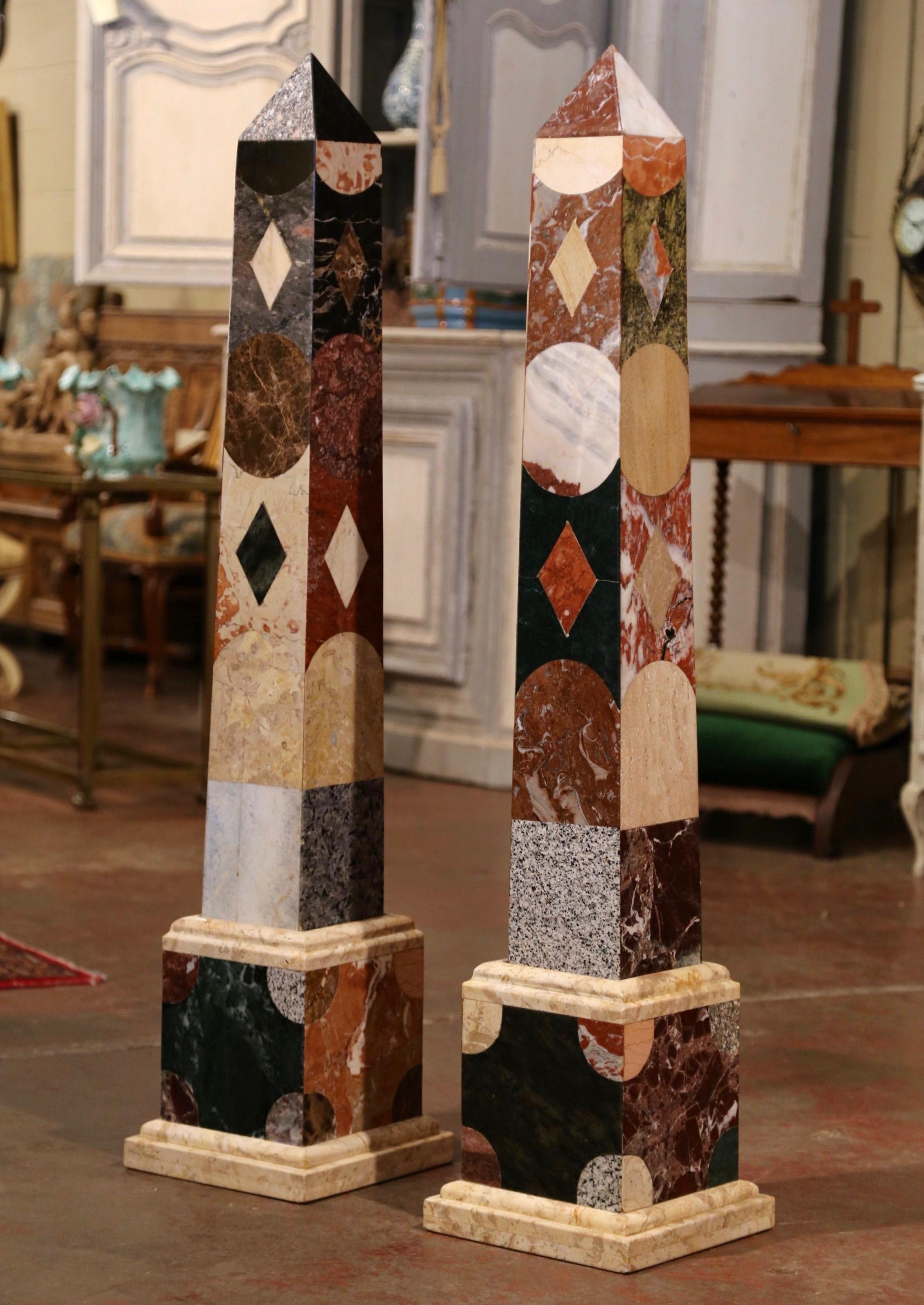 These elegant and monumental Grand Tour marble obelisks were crafted in Italy, circa 1960. Each colorful obelisk stands on a separate conforming square base and features a carved and tapered marble stem embellished with geometric decor. Both pieces