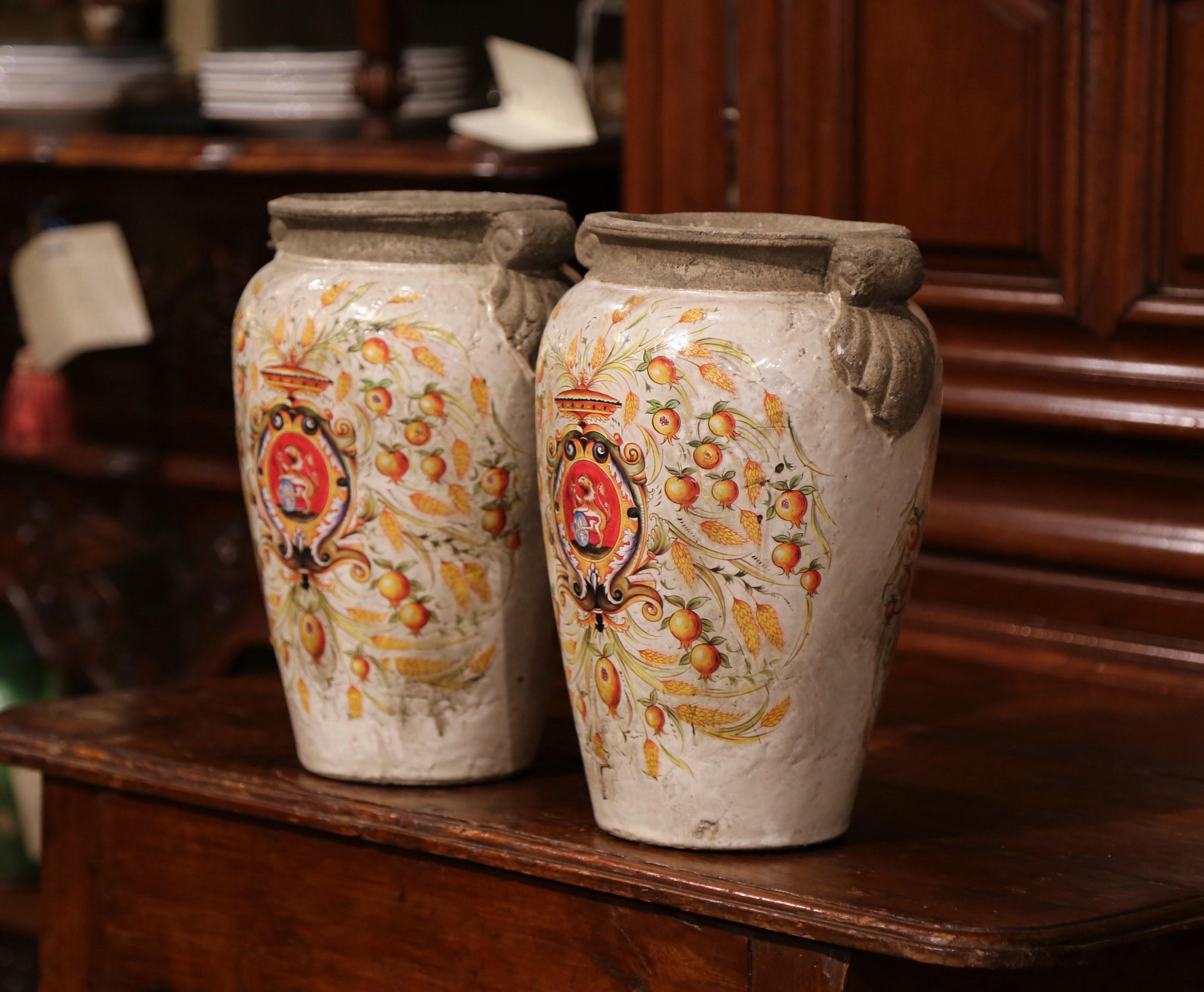 Decorate your mantel with this elegant, colorful pair of vases from Italy. The large, decorative vases are round in shape with small handles on both sides. The ceramic pots feature hand painted colorful decor on both sides, which includes a crest,