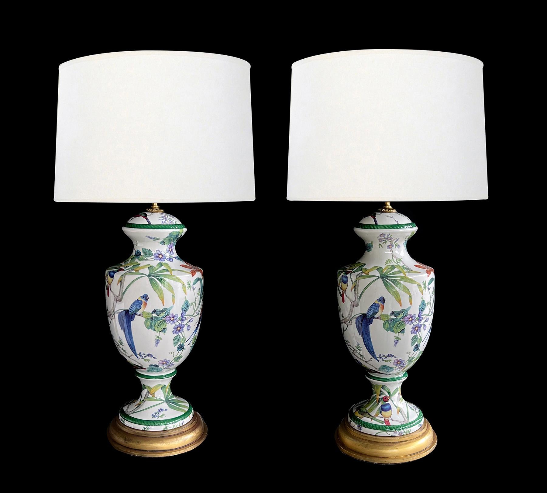 chaque lampe signée par l'artiste est de forme balustre avec un col cintré au-dessus d'un corps ovoïde reposant sur un pied évasé ; reposant sur une base en bois tourné peint à l'or ; chaque lampe est ornée d'oiseaux exotiques bien exécutés et