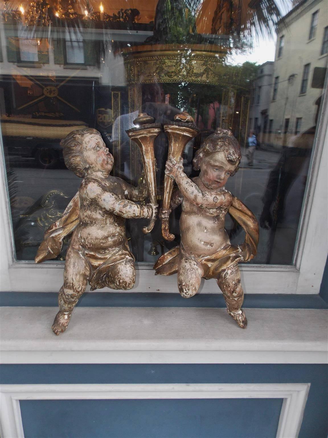 Pair of Italian hanging carved wood, gesso, and poly chromed figural putti each holding a torch, wrapped with a sash, and fitted with exterior rear mounts. Late 18th century.